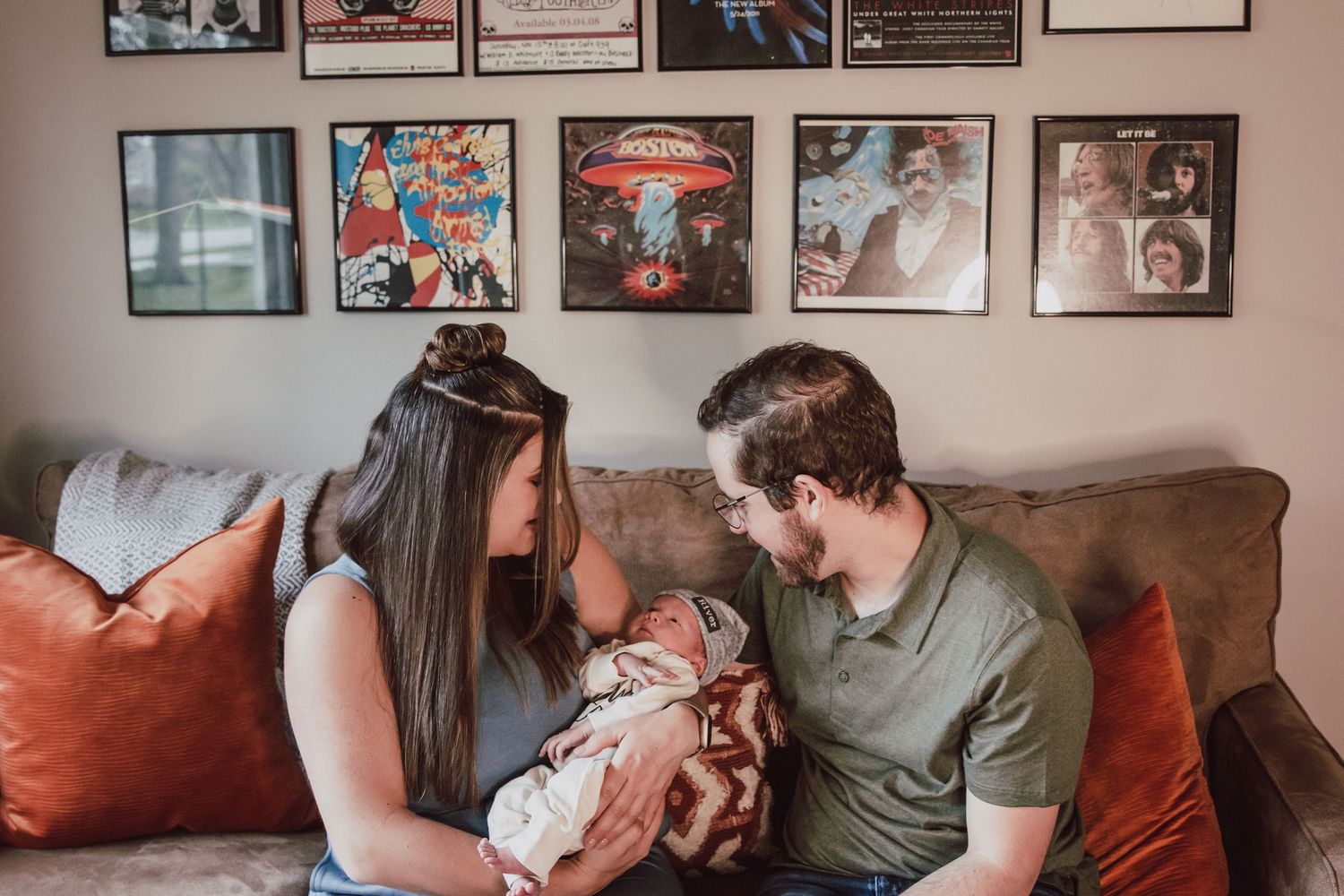 New parents gazing lovingly at their newborn baby on a couch with framed art wall.