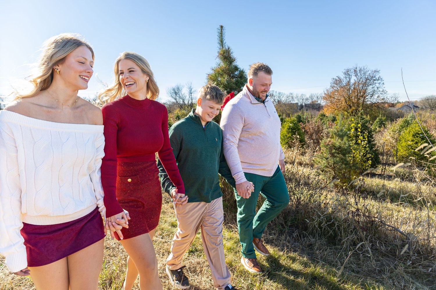 Family of four walking and laughing together at a Christmas tree farm.