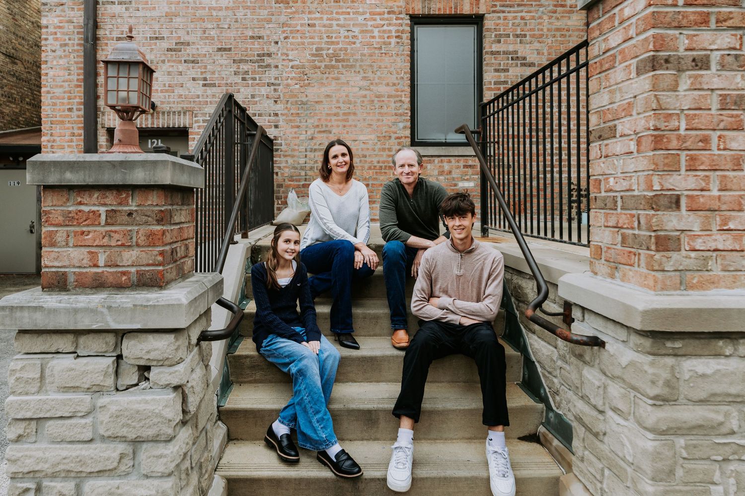 Family of four smiling on brick building steps in casual attire.