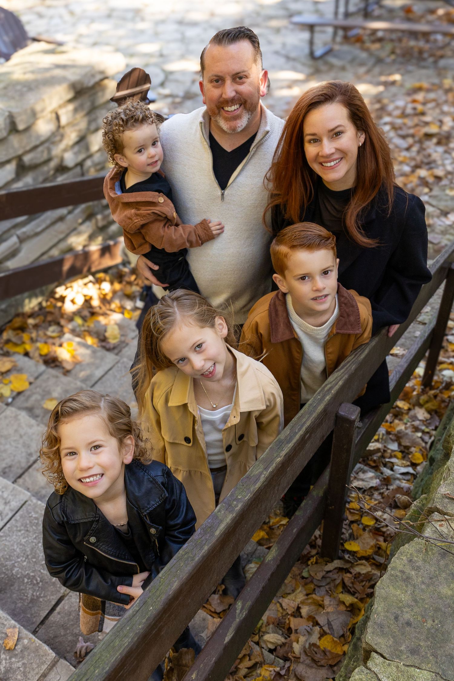 Smiling family of six posing on stone steps surrounded by autumn foliage.