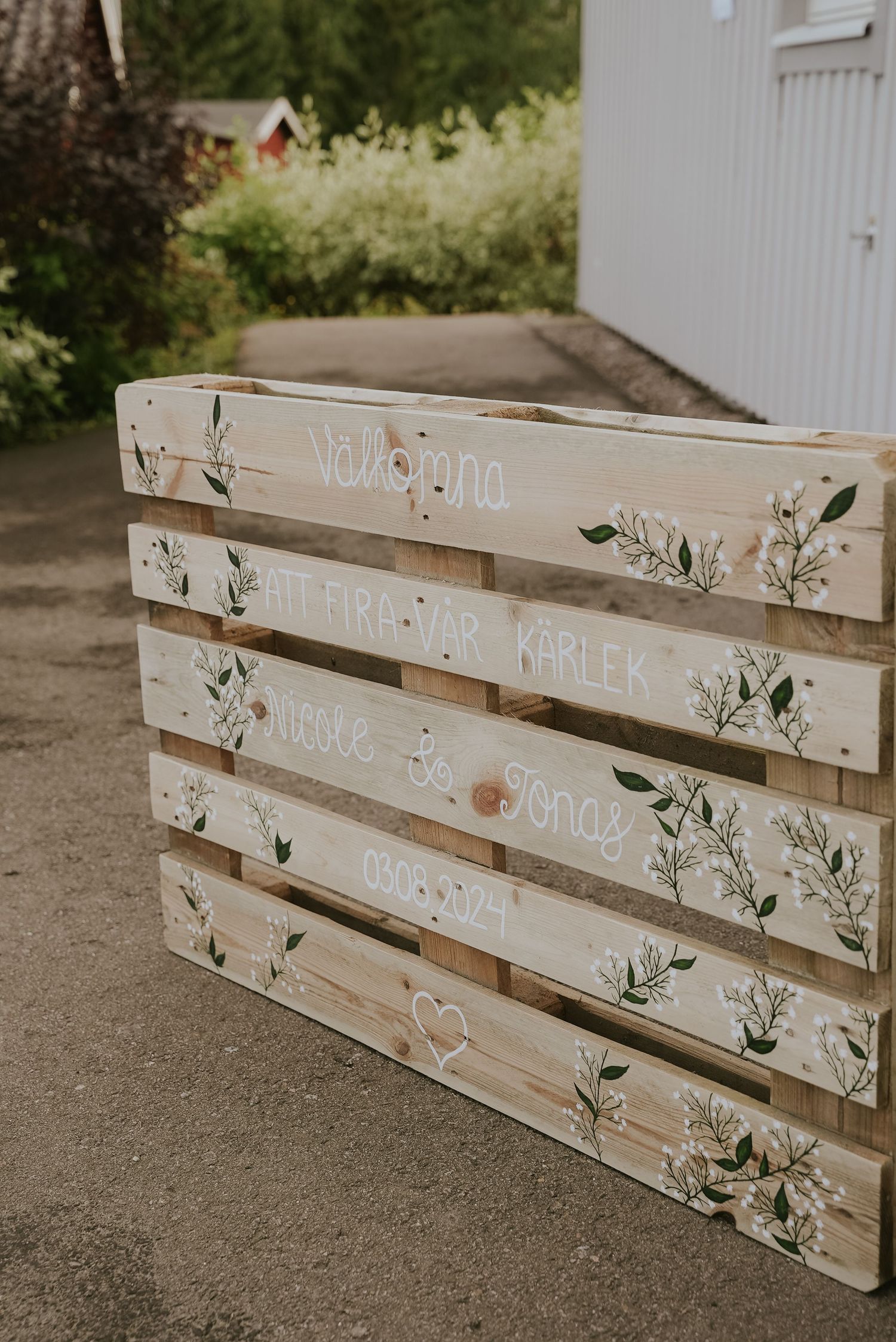 Rustic white wooden pallets decorated with hand-painted floral designs and text displayed outdoors.