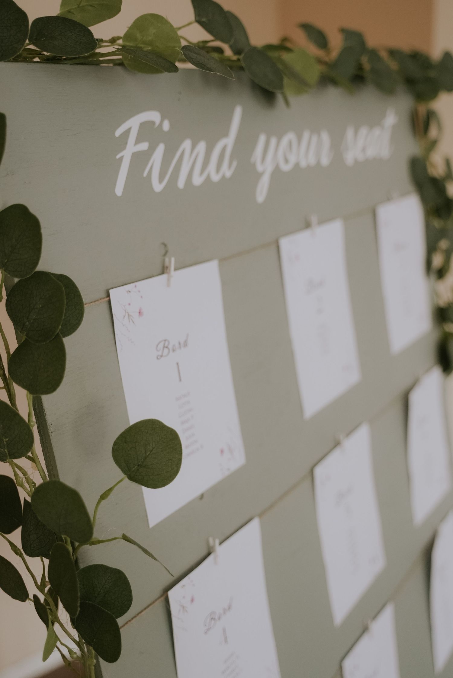 White seating cards arranged on a wall with green foliage decorations for an elegant wedding reception.