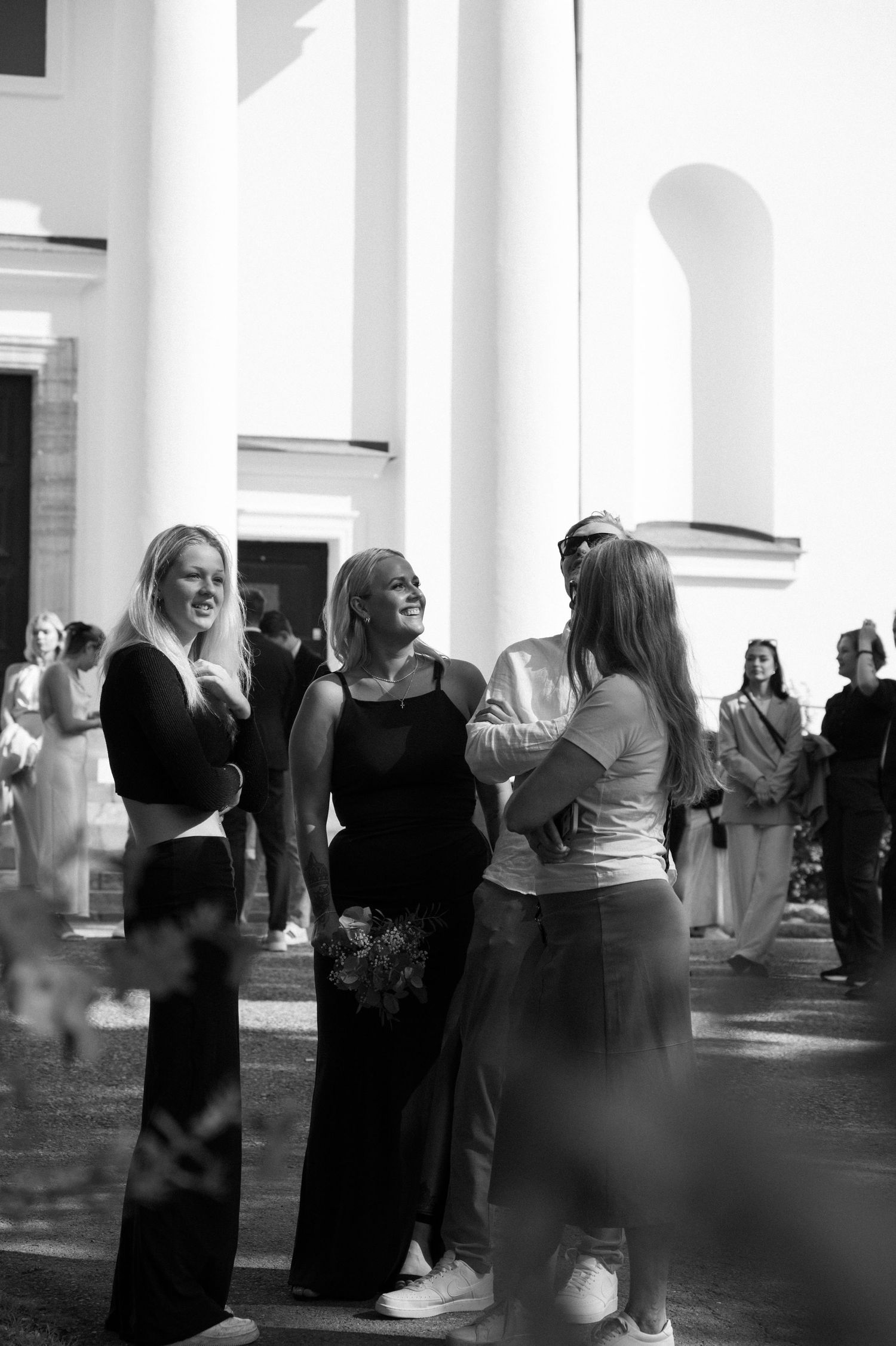 Wedding guests mingle beneath white columns in an elegant black and white scene.