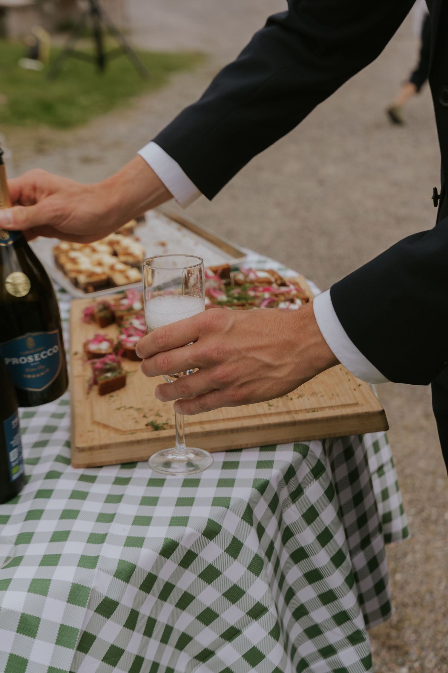 Close-up of hands preparing charcuterie on wooden boards with a checkered tablecloth.