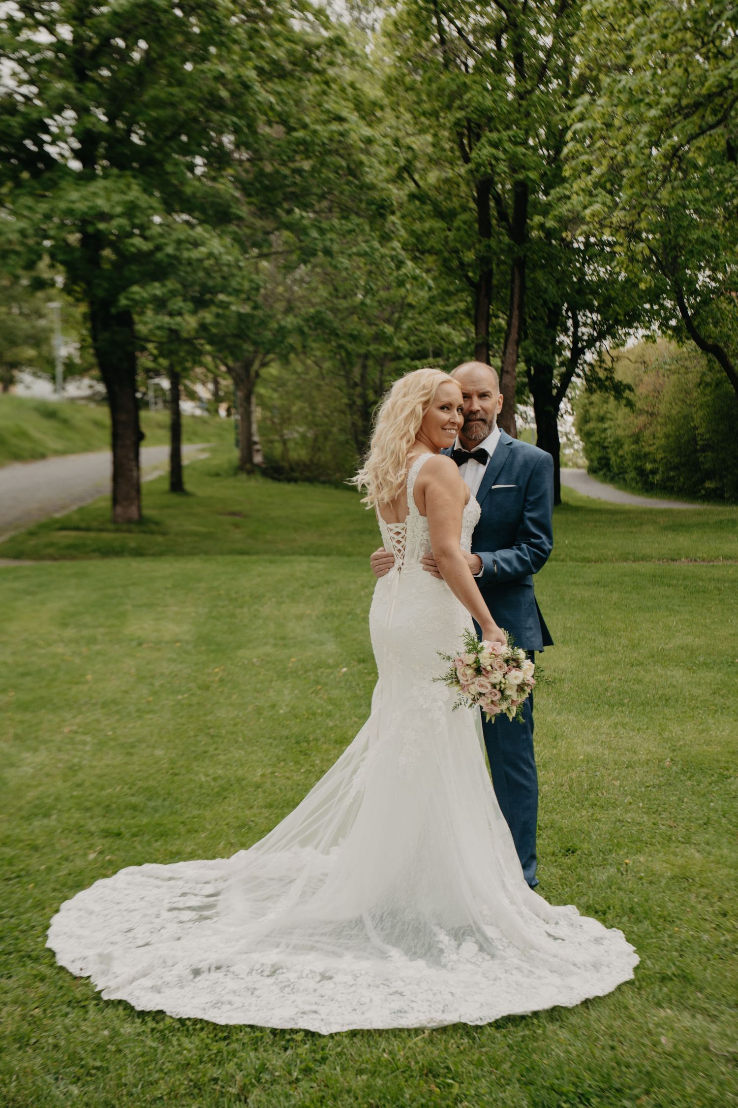 Wedding portrait in park setting showing couple with flowing lace train spread on green grass.