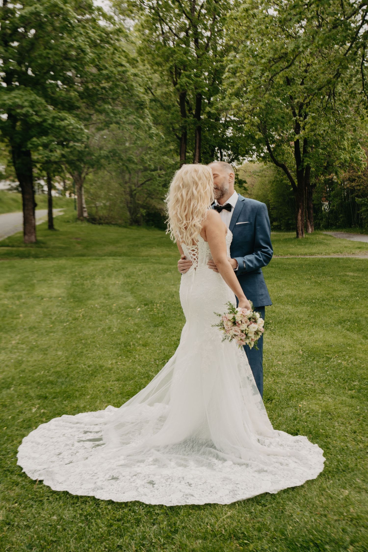 Wedding couple standing together on grass with bride's elegant lace train spread behind them.