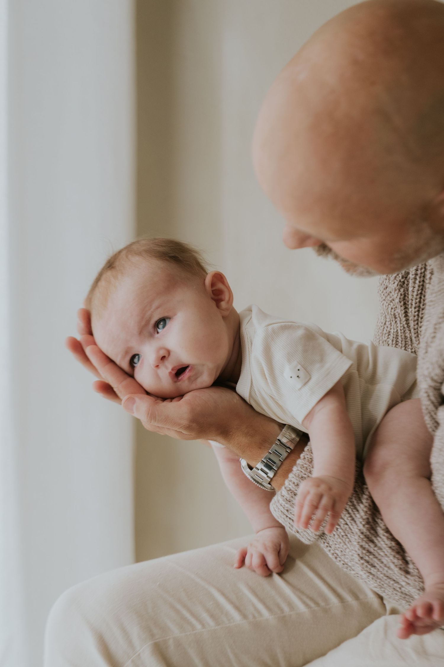 Gentle newborn photography showing baby being cradled in natural light setting.