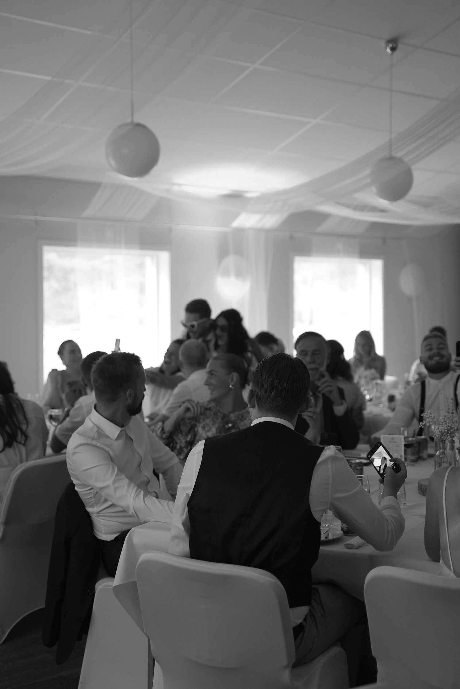 Wedding guests enjoy a reception celebration in an elegant white room with round paper lantern decorations.