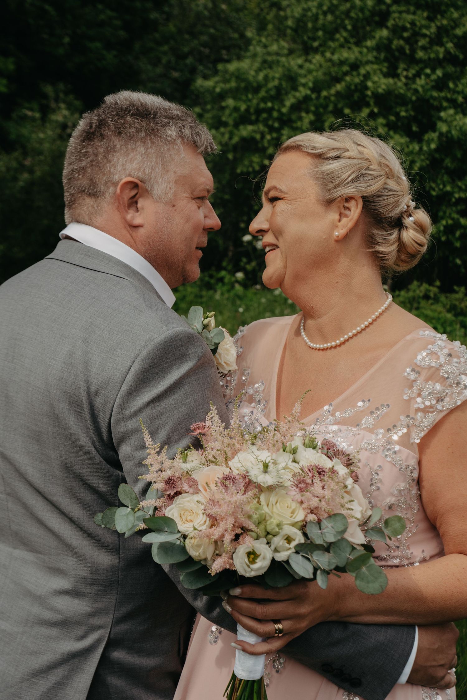 A couple shares a joyful moment with a pink and white floral bouquet during their wedding.