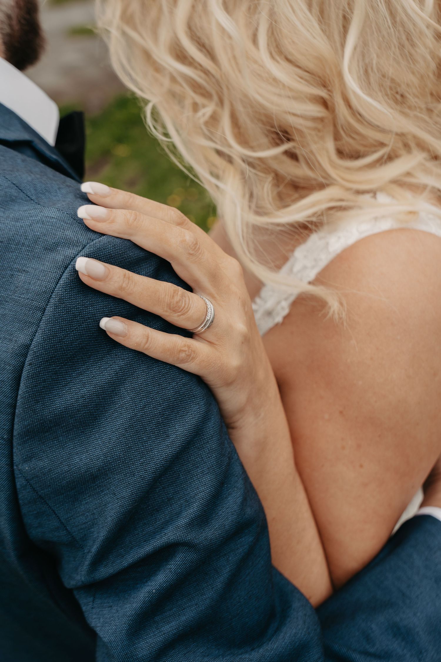 Close-up detail of hands with wedding ring against a navy suit jacket.