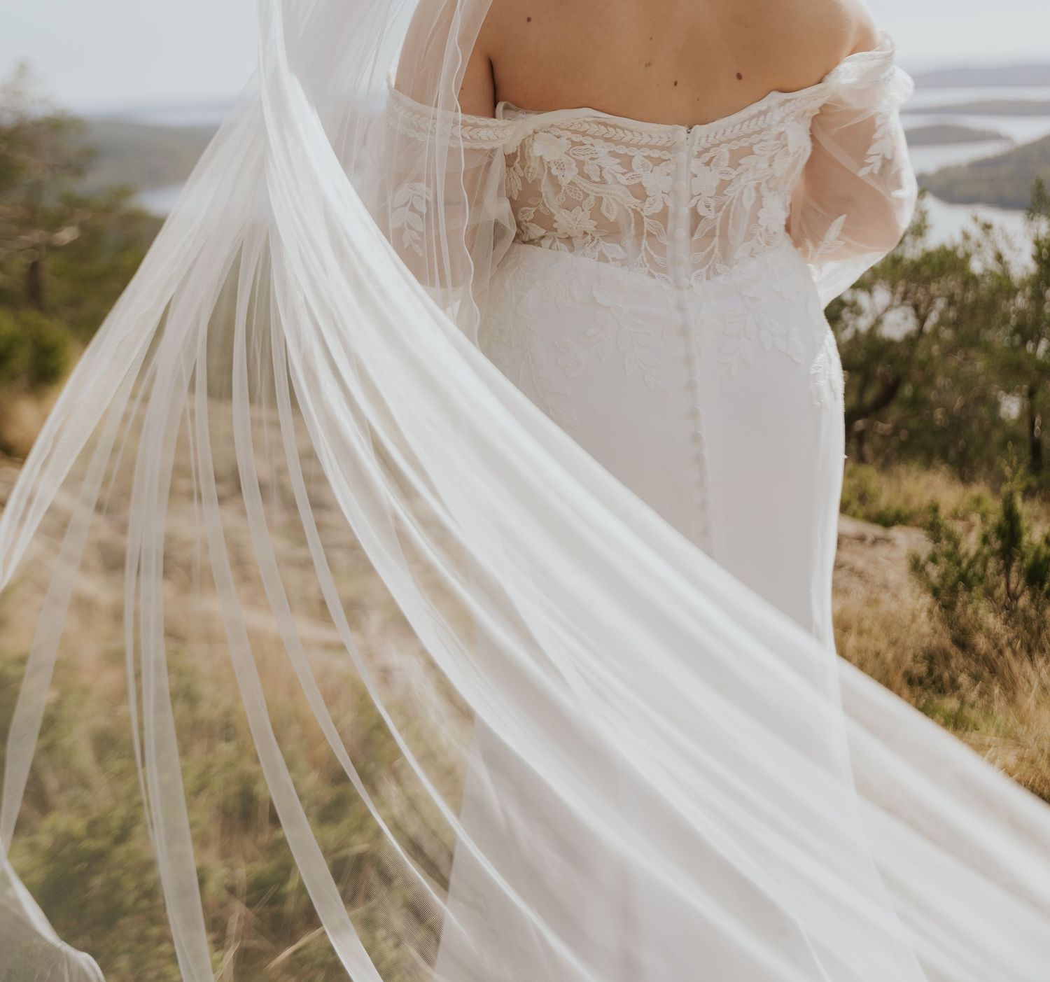 Flowing white wedding veil billows dramatically in the wind against a natural landscape.