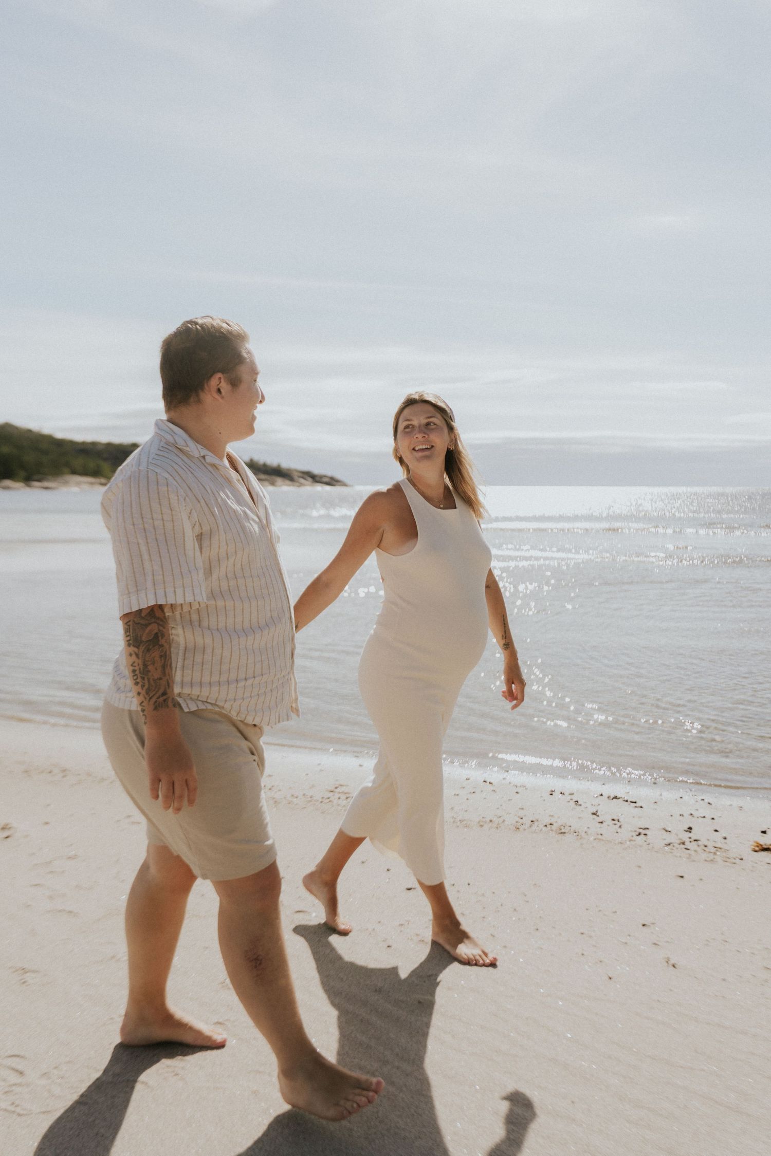Couple walking playfully along beach shoreline in casual summer outfits.