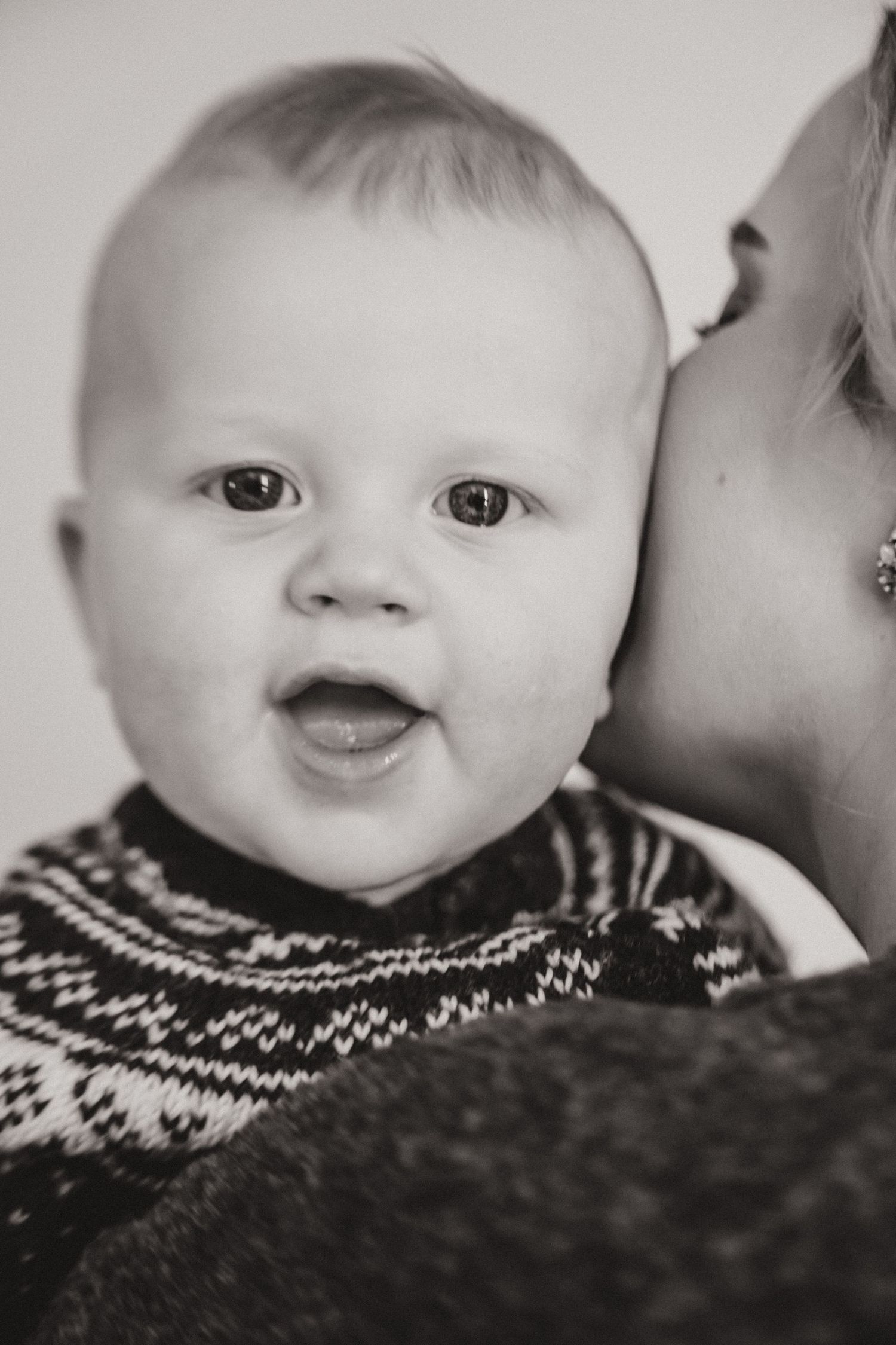 A close-up black and white portrait of a baby wearing a patterned sweater.