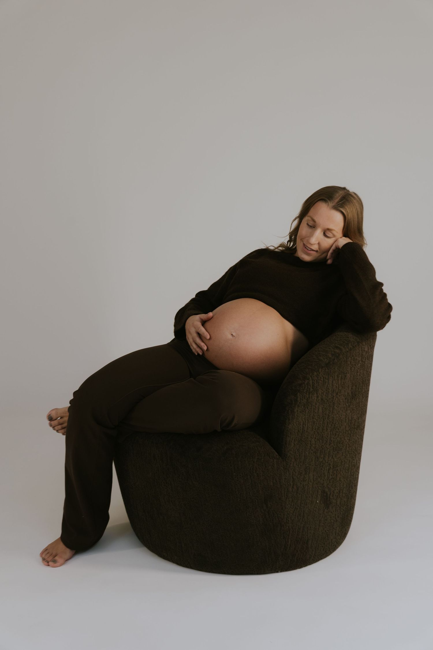 Artistic maternity photos showing relaxed poses on a dark chair against grey background.