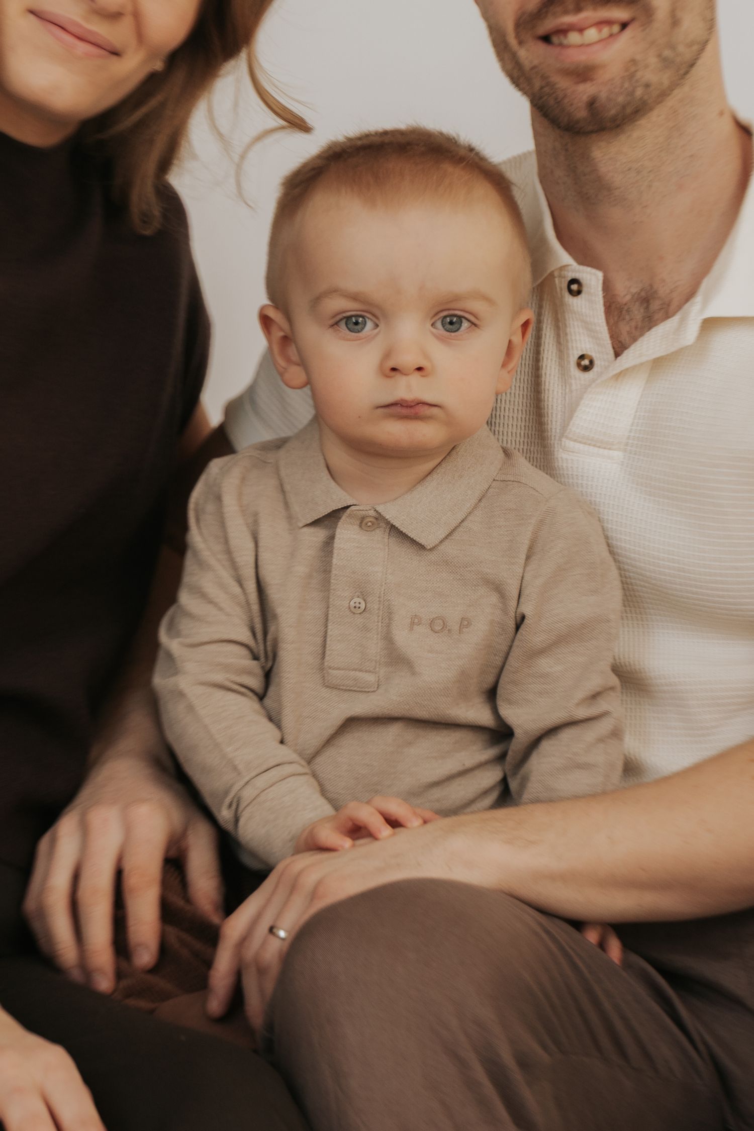 A young child in a beige collared shirt sits on someone's lap in a warm-toned studio portrait series.