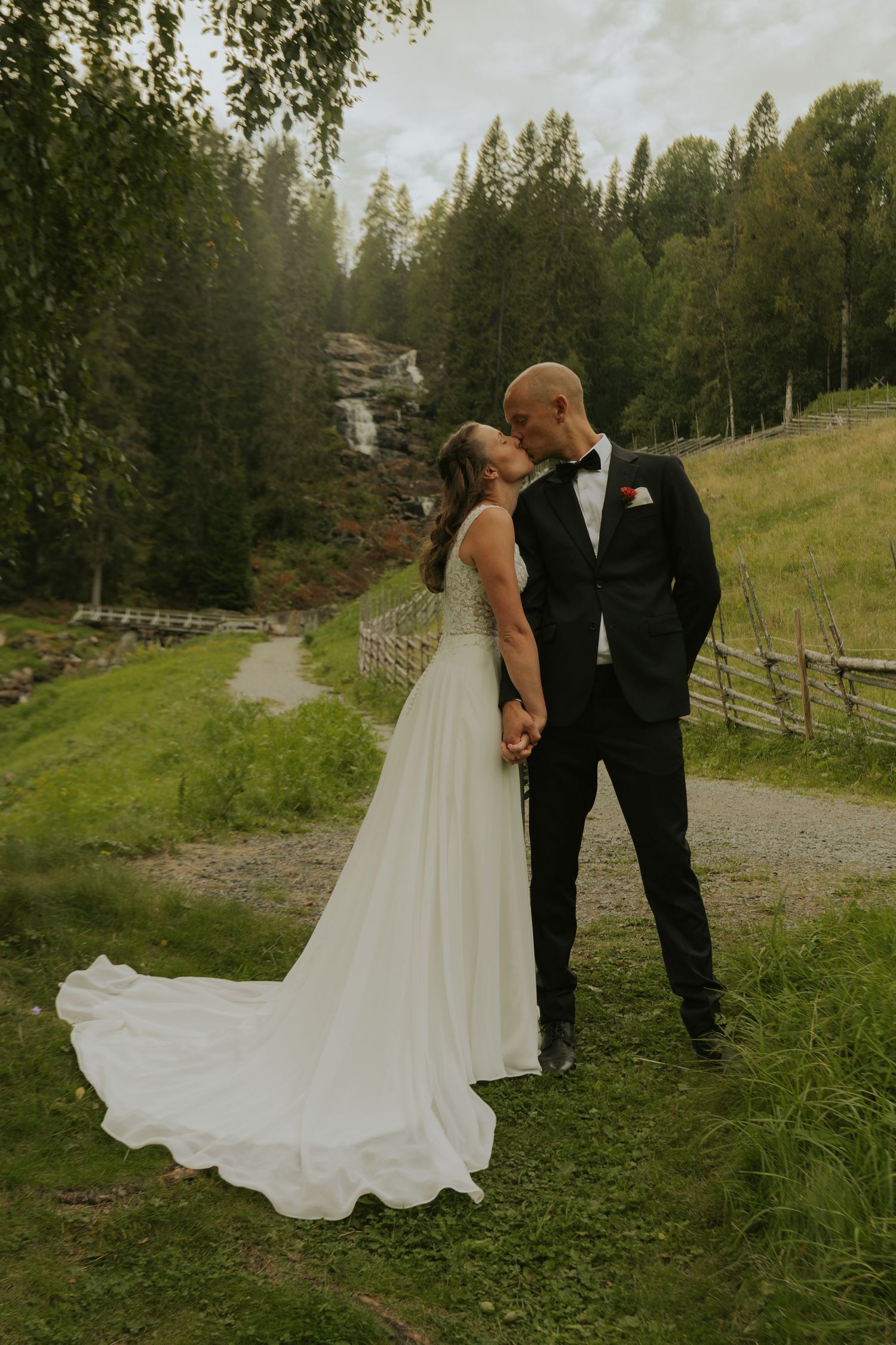 Wedding couple sharing intimate moments on mountain path with evergreen forest backdrop.