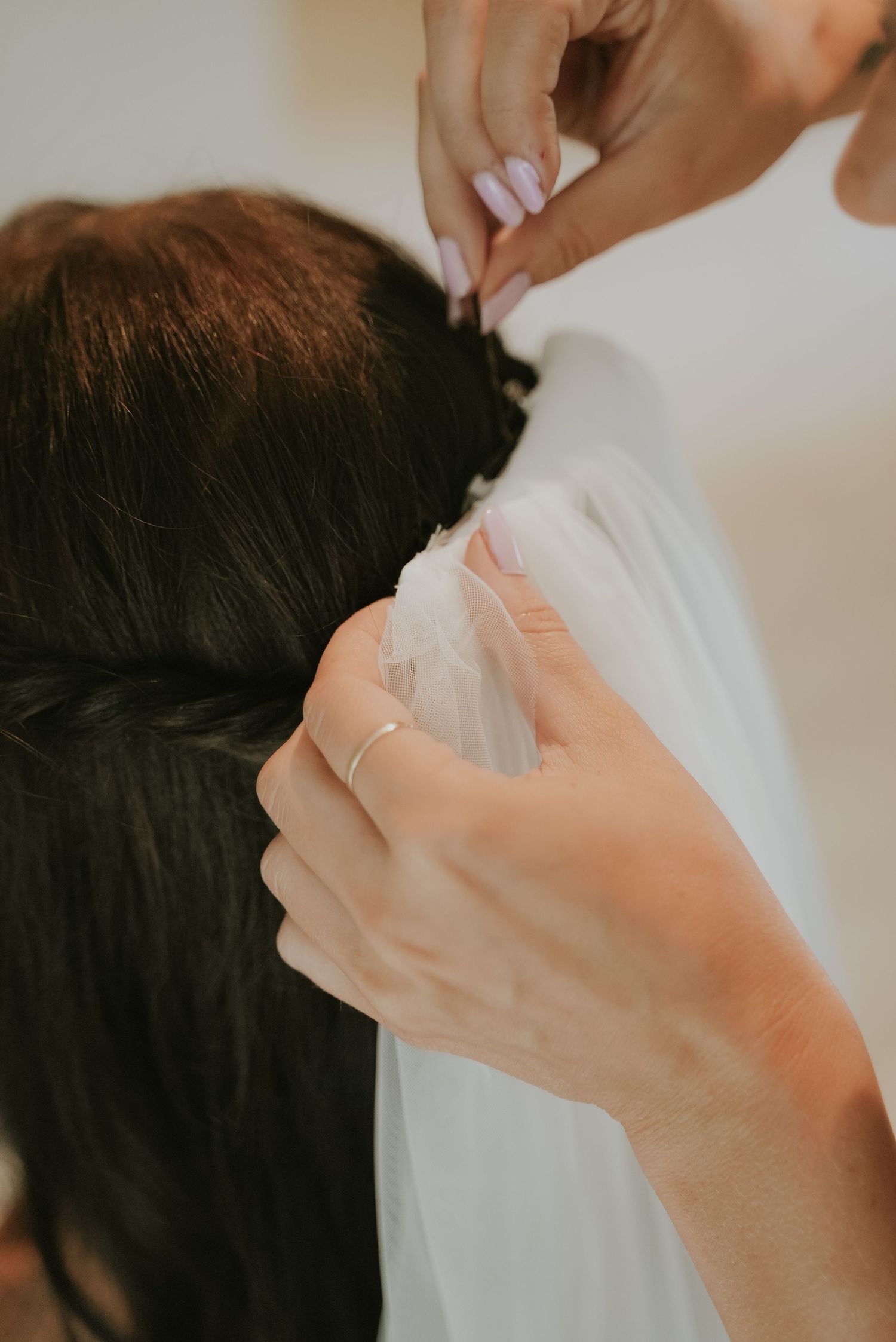 Close up view of hands adjusting a white veil on dark hair during wedding preparations.