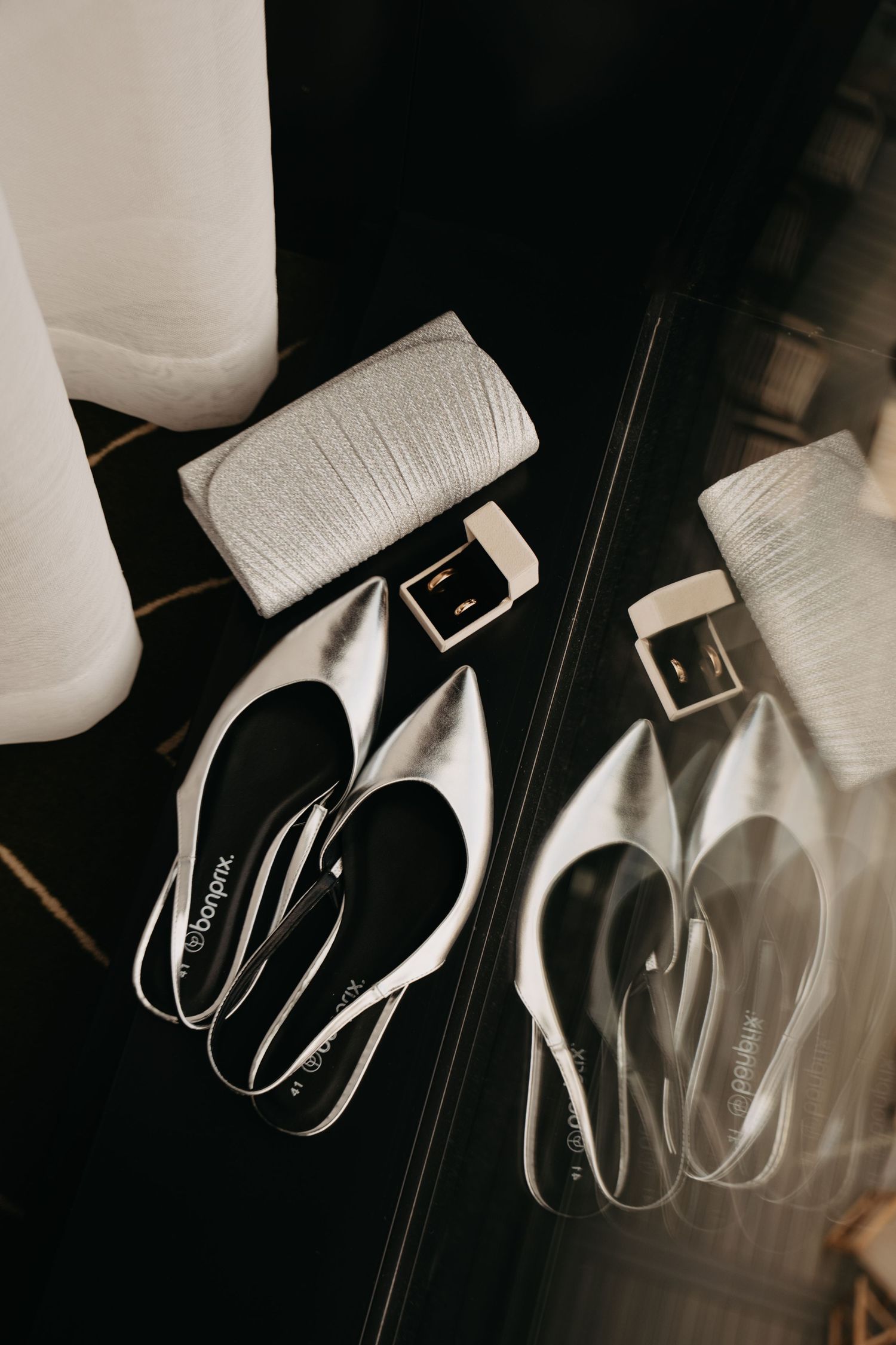 White bridal shoes and clutch arranged on dark surface with reflective mirror.