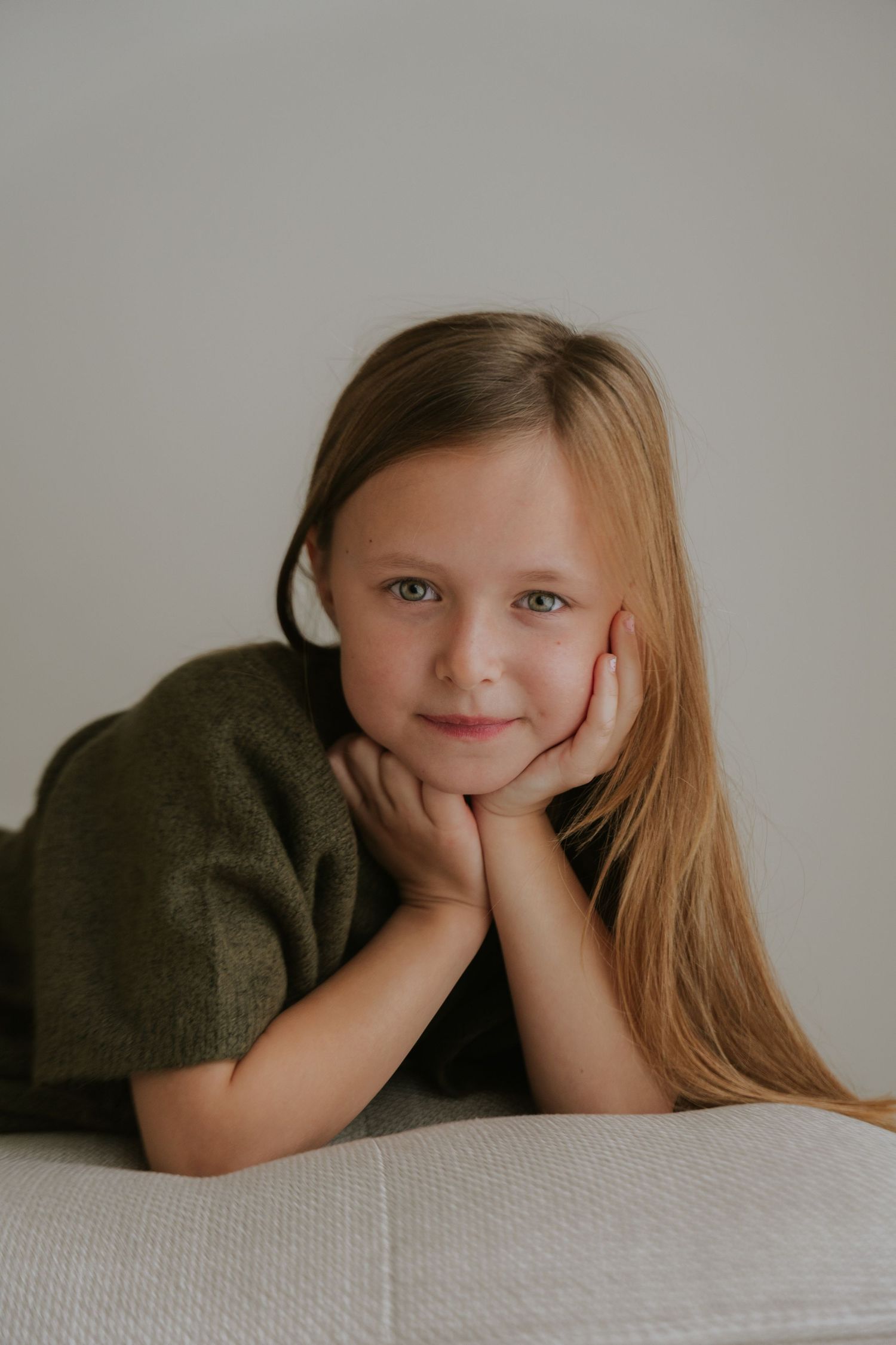 Child resting head on hands while laying on white surface in artistic portrait series.