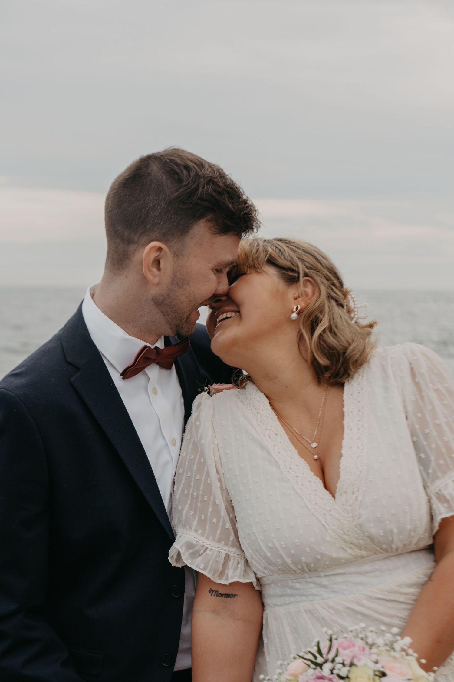 Candid wedding portraits capture joyful laughter between newlyweds on rocky beach.