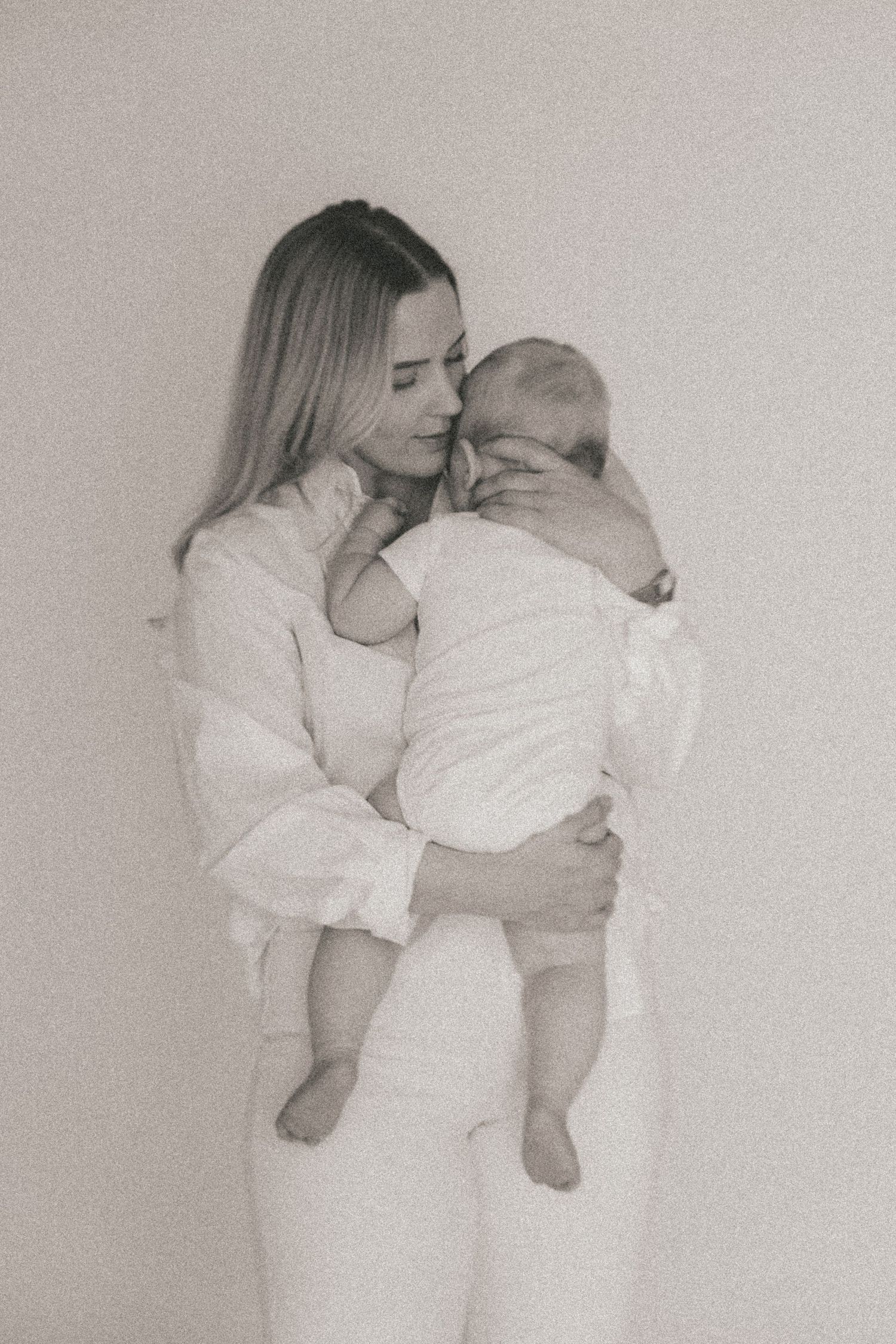 Intimate black and white portrait of parent holding baby in matching white outfits.