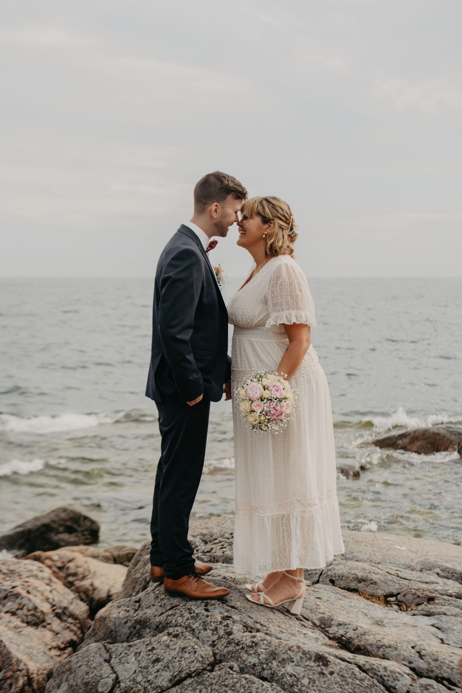 Wedding couple shares intimate moments while standing on dramatic rocky coastline.