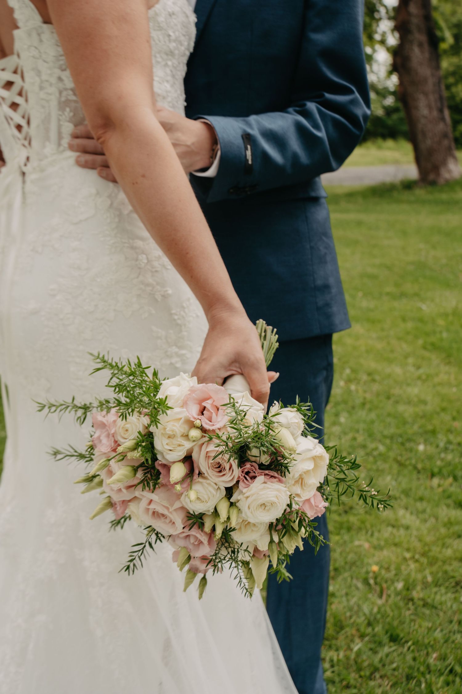 Wedding bouquet with blush roses and greenery held against white lace gown.