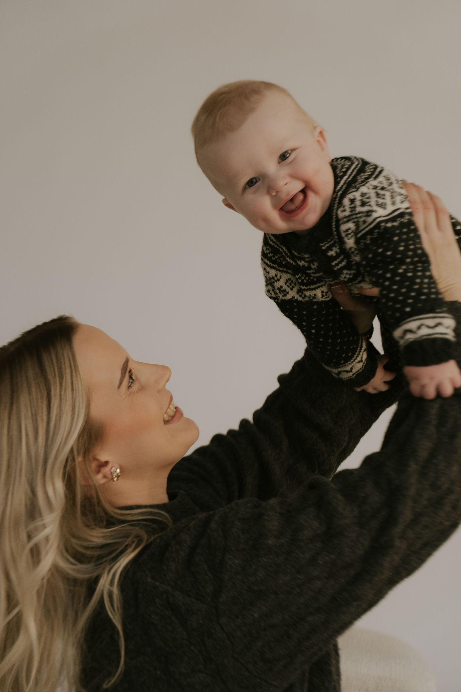 A joyful indoor portrait showing a baby wearing a patterned sweater being lifted up.