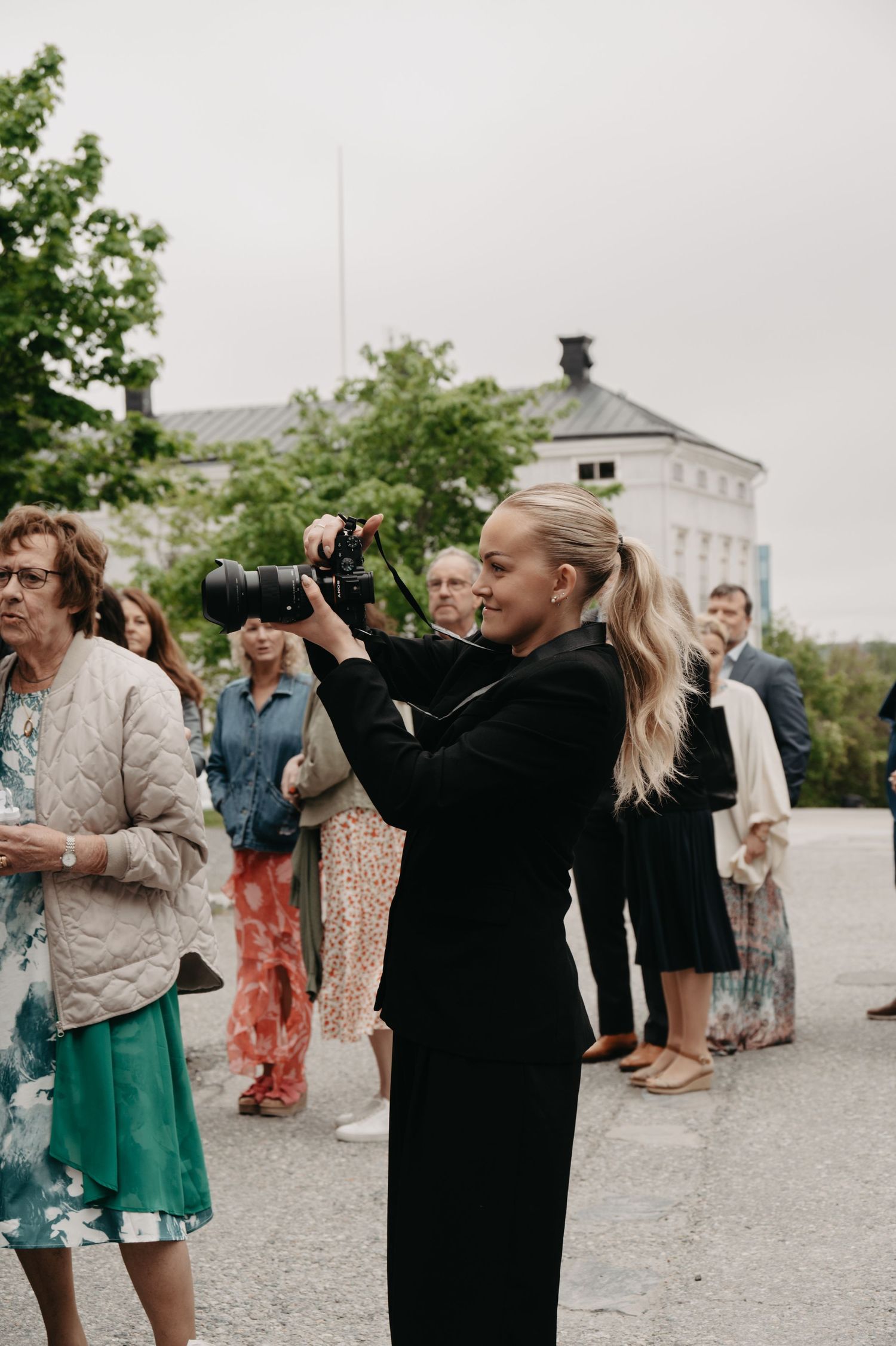 Wedding guests in colorful dresses gather outdoors taking photos during a celebration.