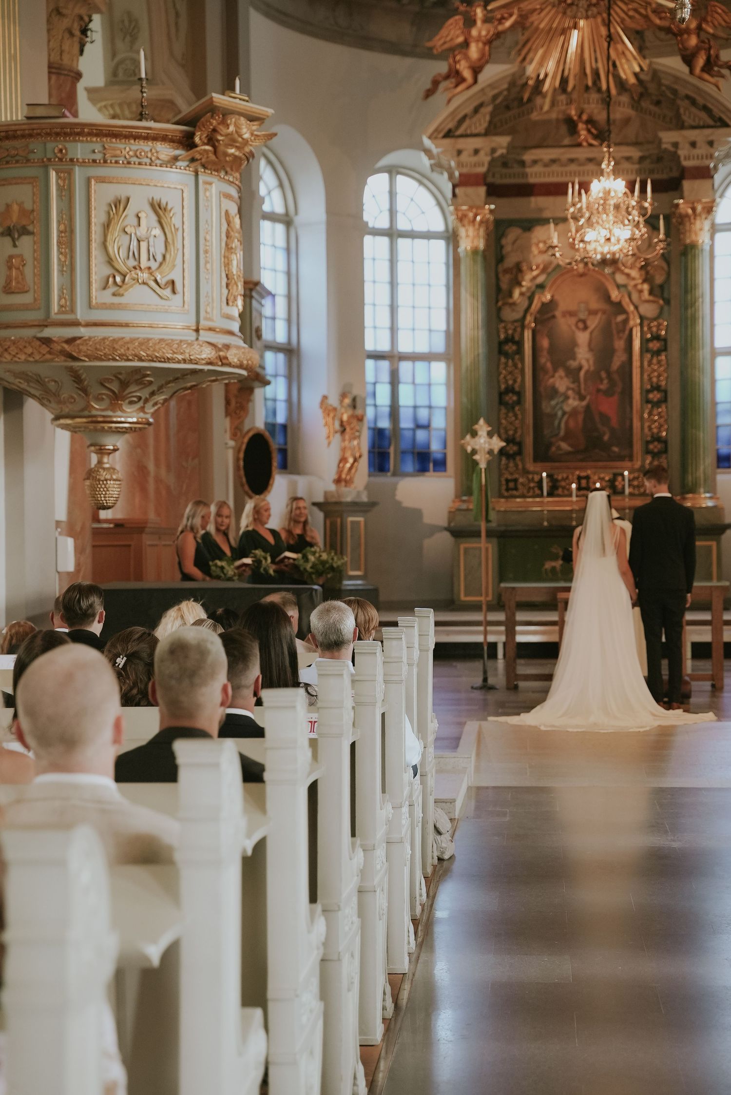 A panoramic view of an elegant church interior with white pews and ornate baroque decorations during a wedding ceremony.