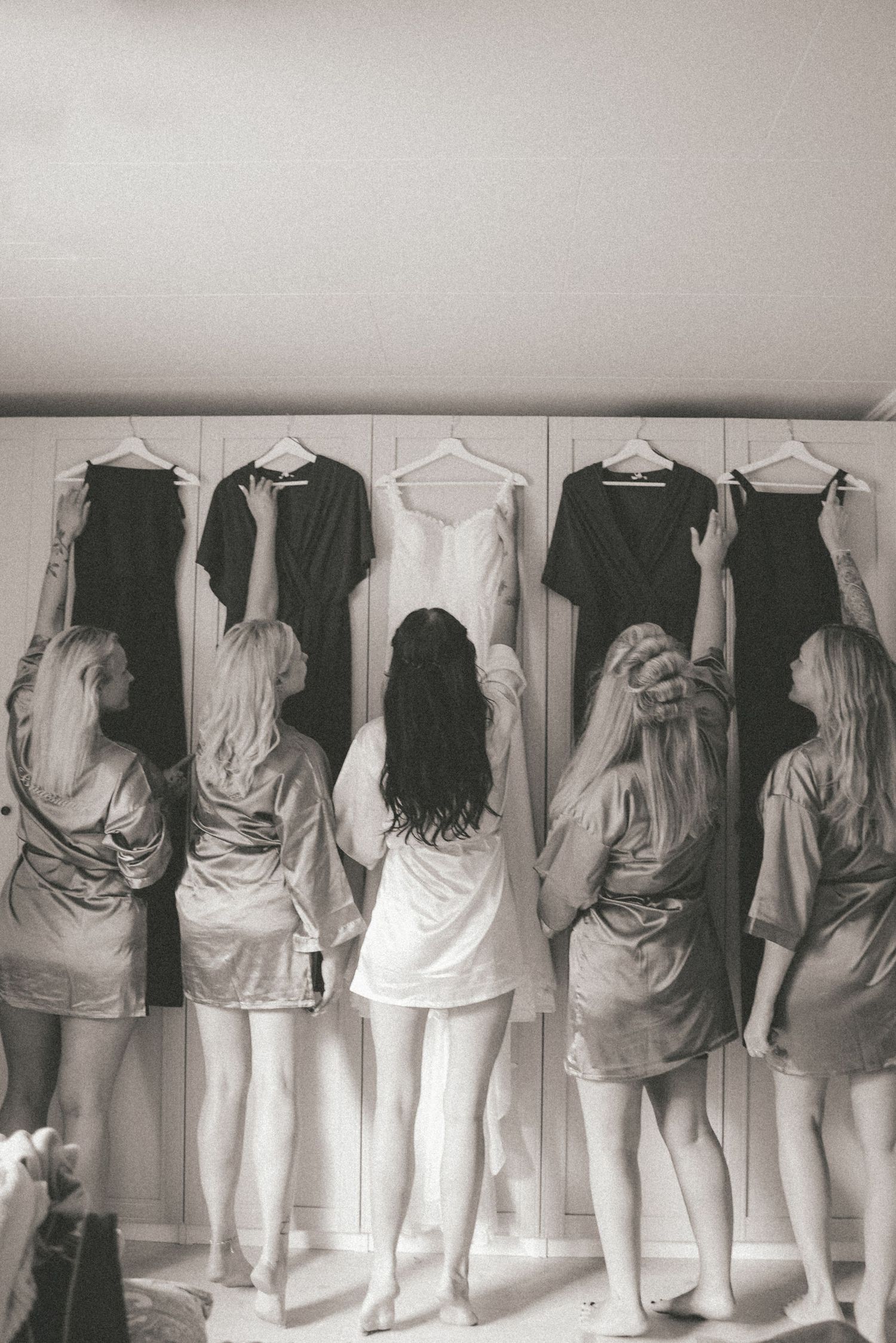 A black and white artistic photograph showing a line of people facing a wall wearing white and dark clothing.