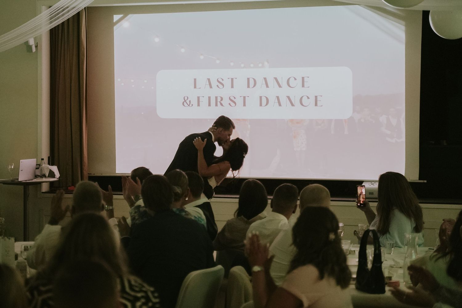 Wedding guests dance together on a dimly lit dance floor during a reception celebration.