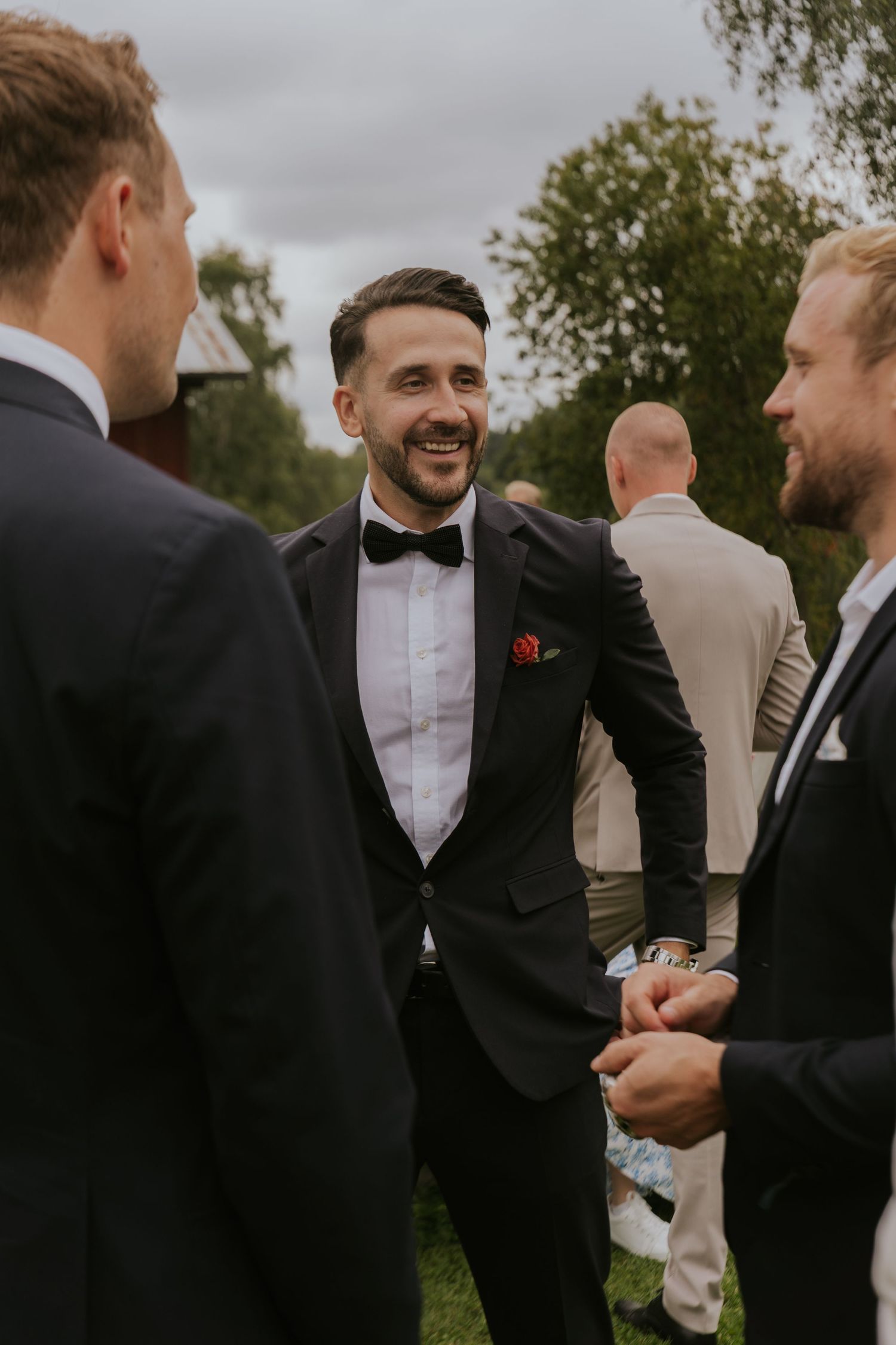 Three men in formal attire share a conversation at an outdoor event.