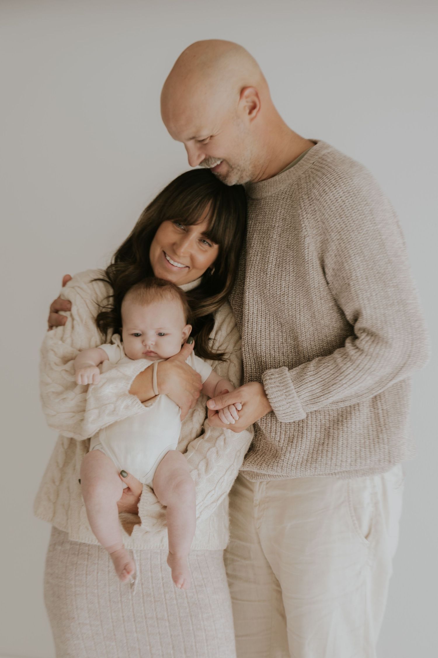 Tender family moment captured in soft lighting with parents embracing baby.
