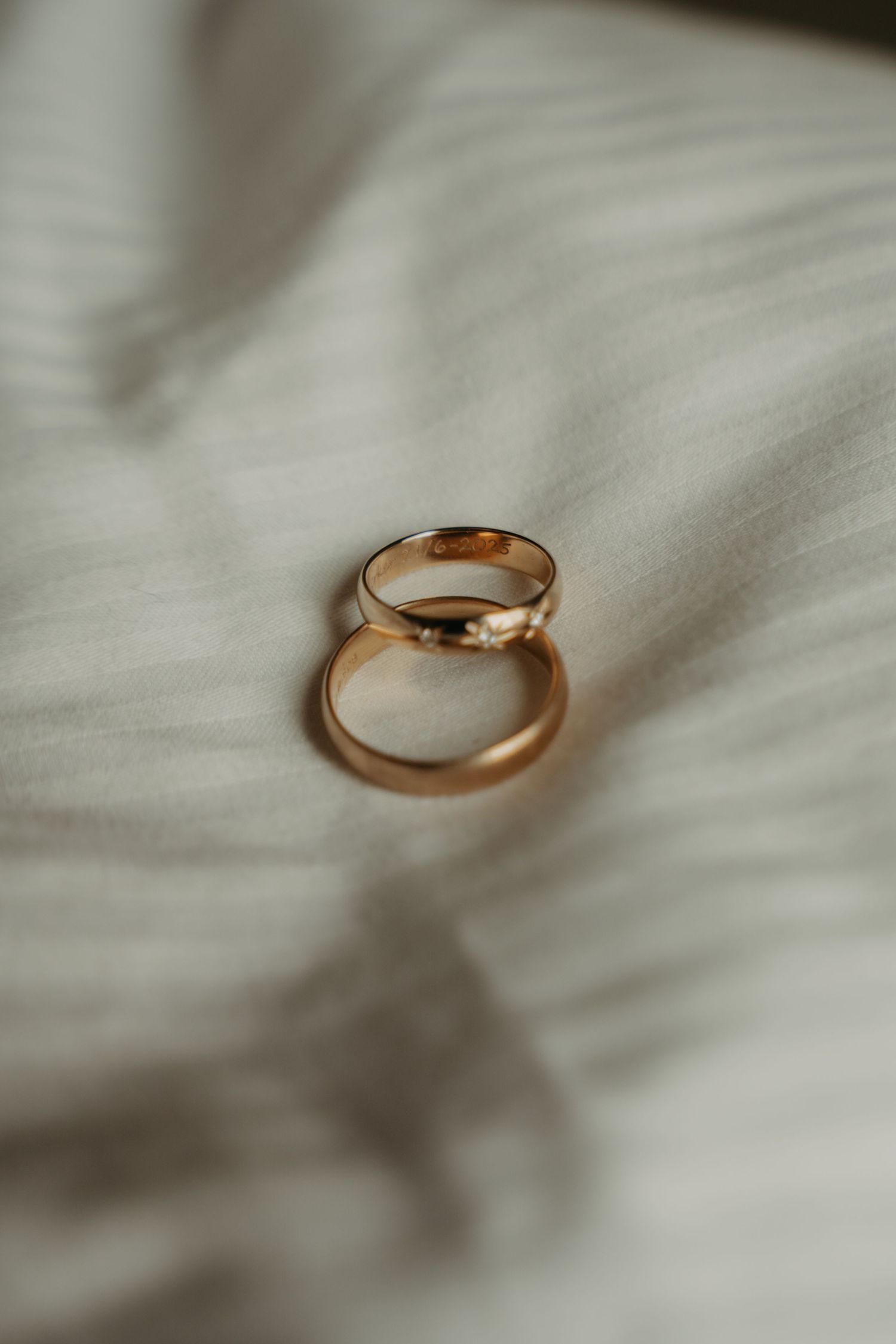 Gold wedding ring photographed on white textured fabric with soft shadows.