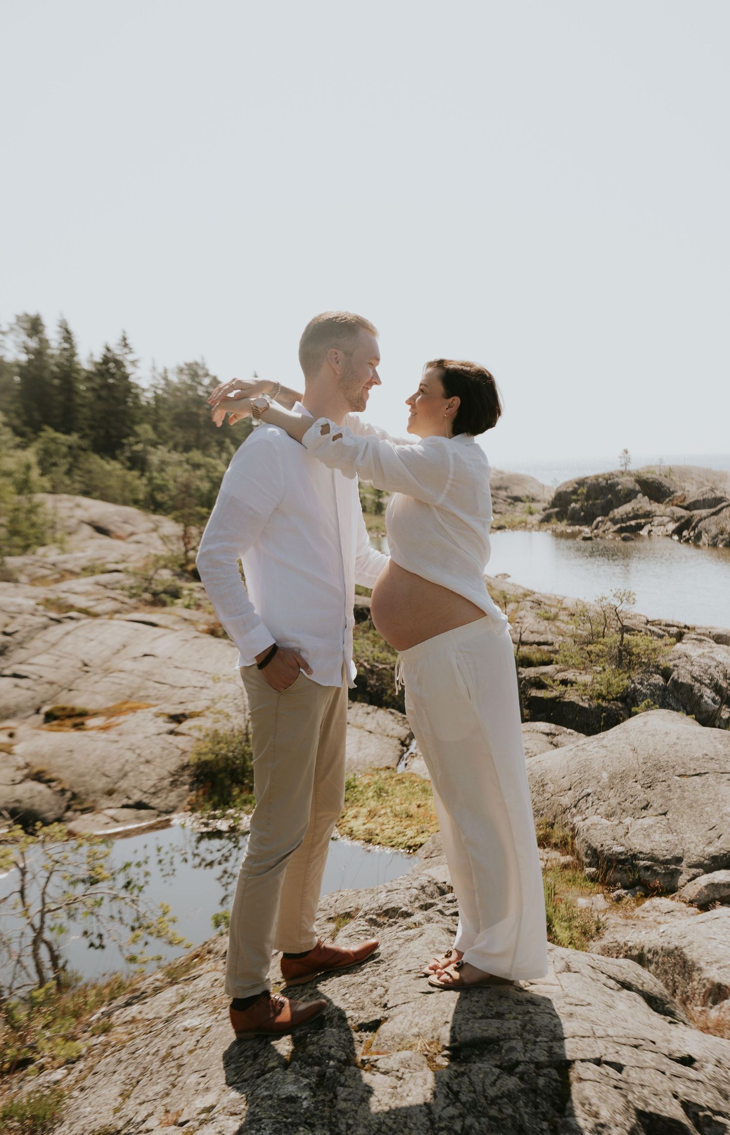 Couple in white shirts and khaki pants standing together on rocky coastal terrain.