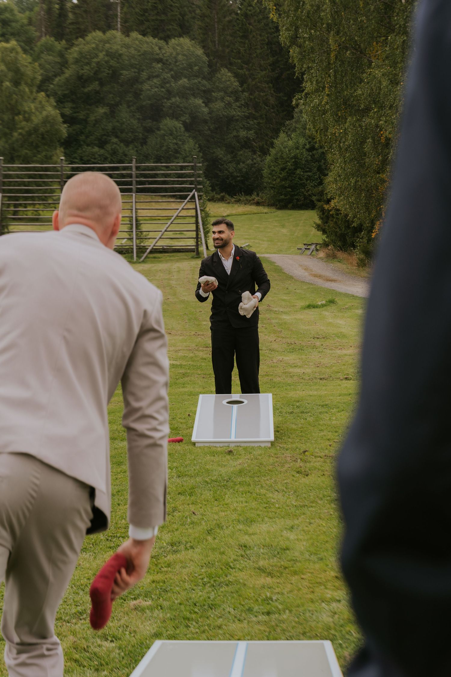 Two people play cornhole on a grassy field during an outdoor event.