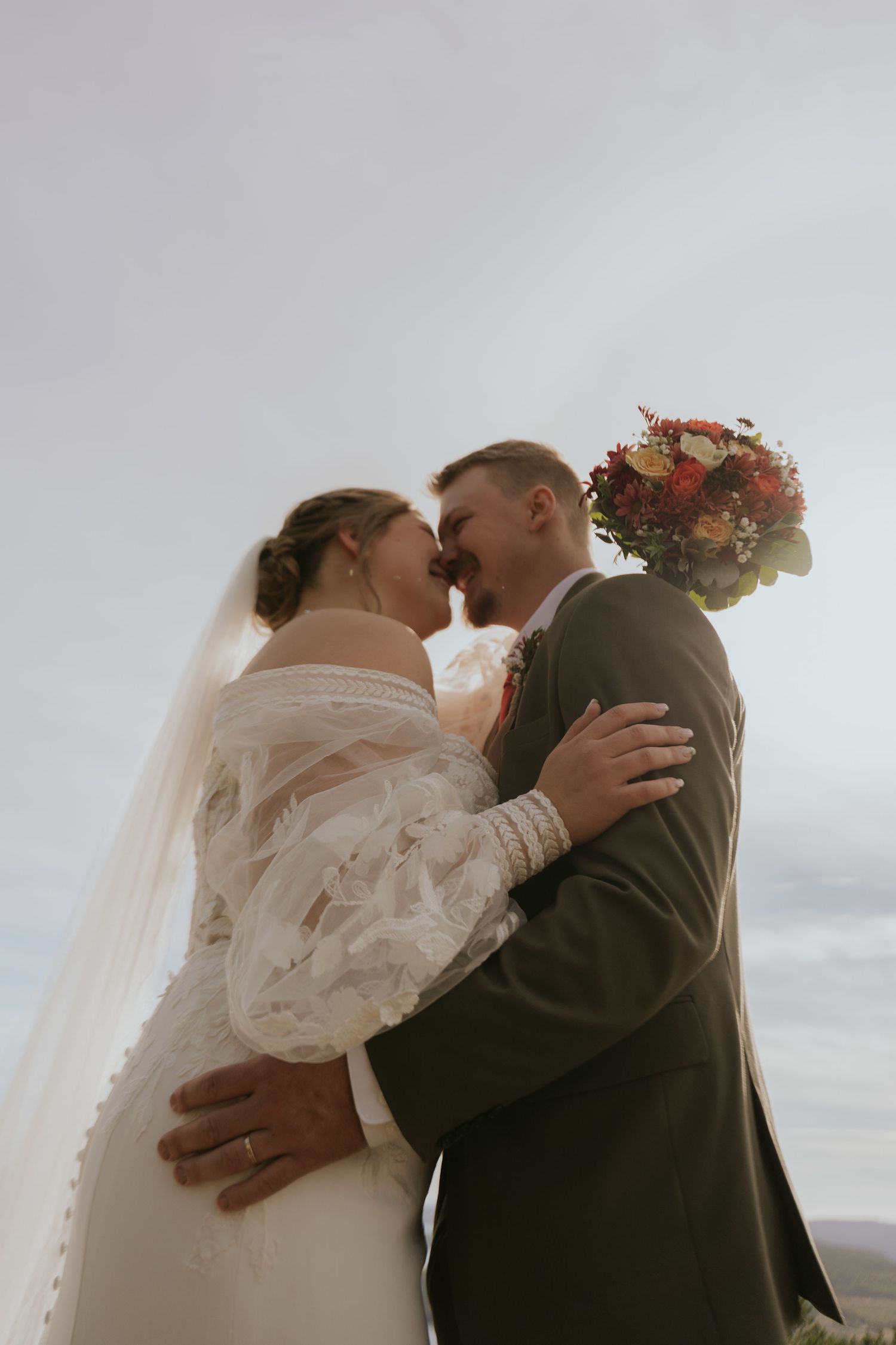 Wedding couple shares romantic kisses against a cloudy sky backdrop.