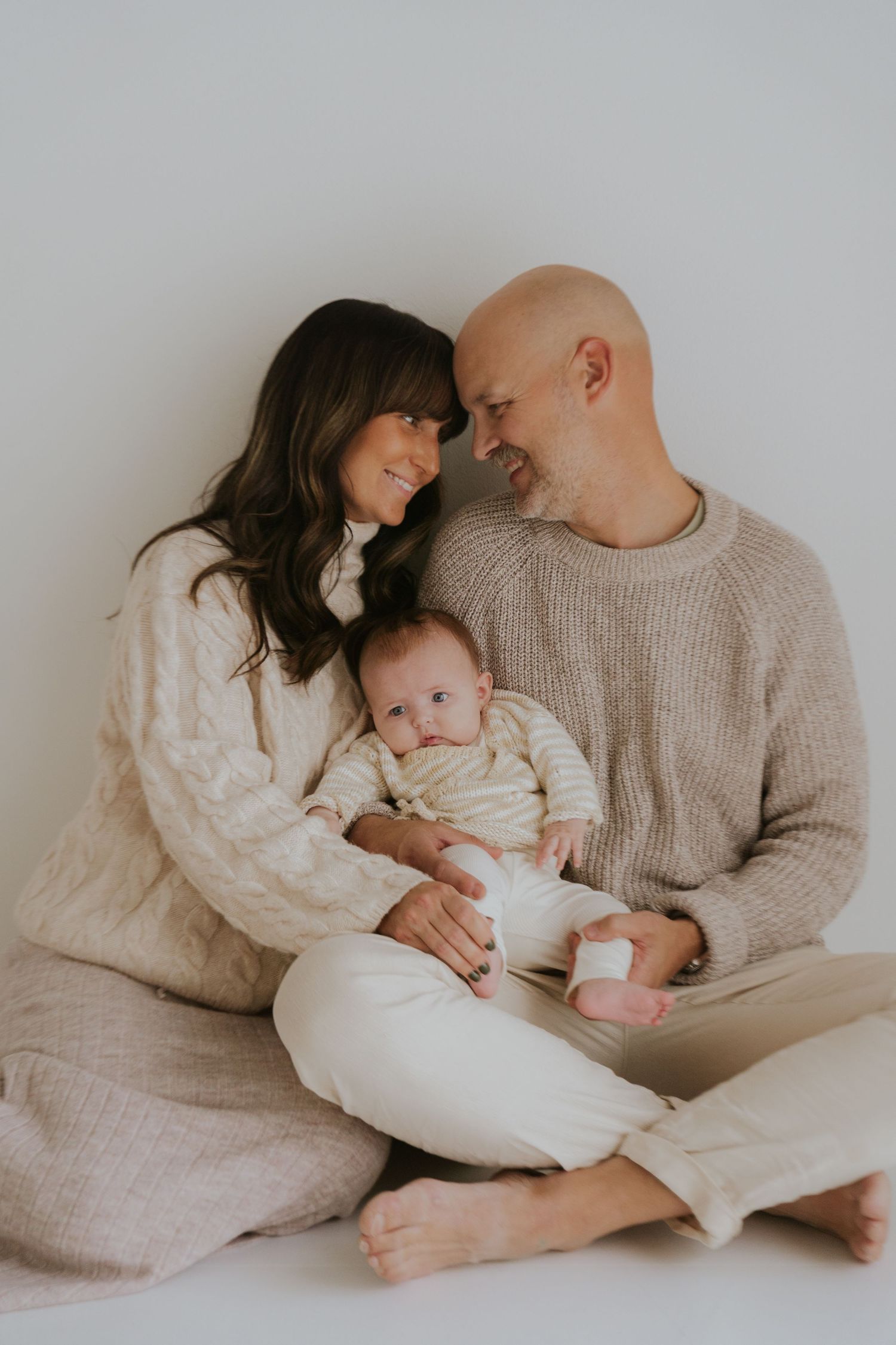 Candid family moment captured in soft lighting with parents and baby relaxing together.