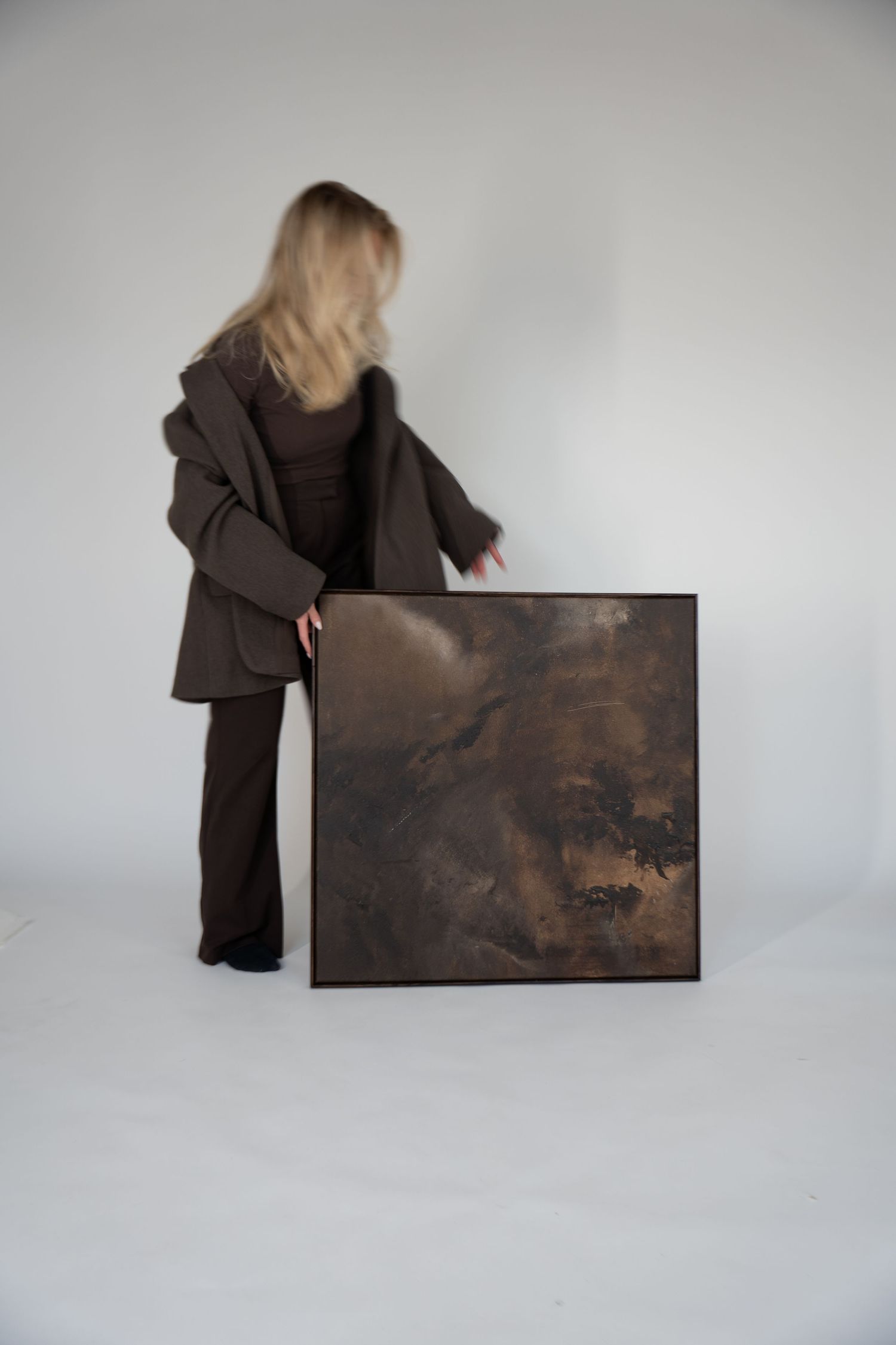 A figure in dark clothing stands beside a large abstract artwork displayed against a light gray background.