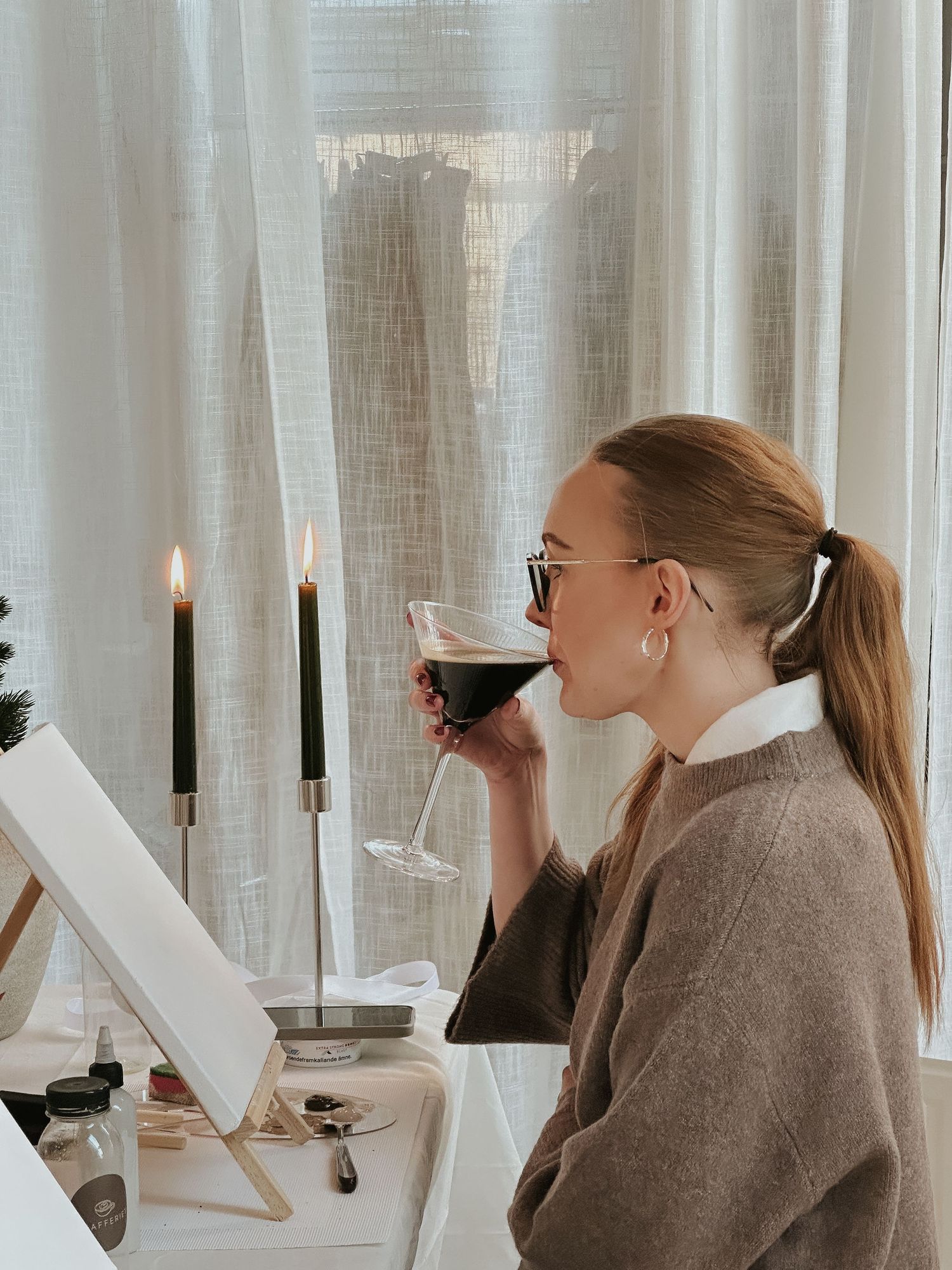 Two people in gray sweaters sit at a white table with candles and wine glasses in a bright minimalist setting.