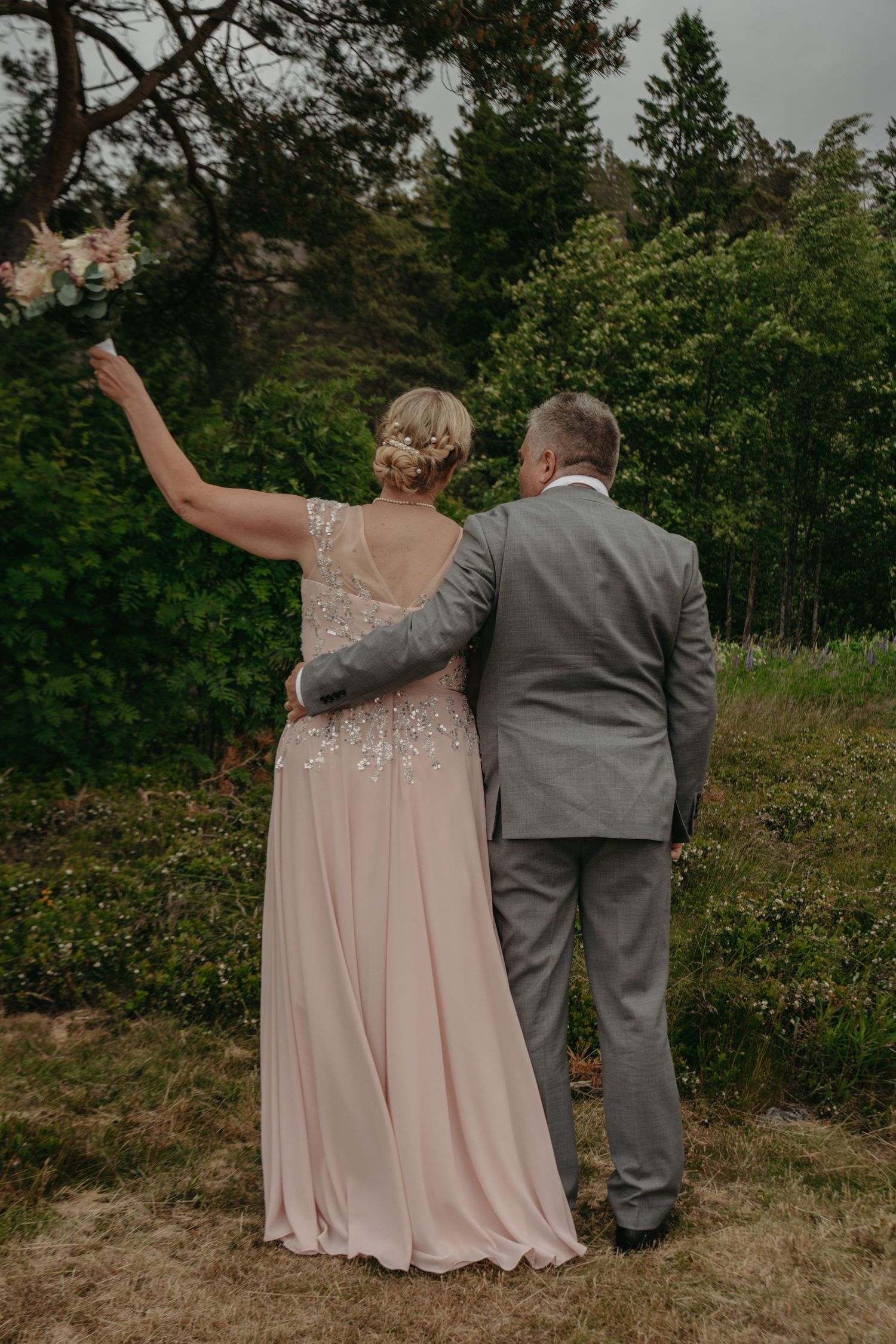 A couple in wedding attire embraces while looking out over a scenic landscape.
