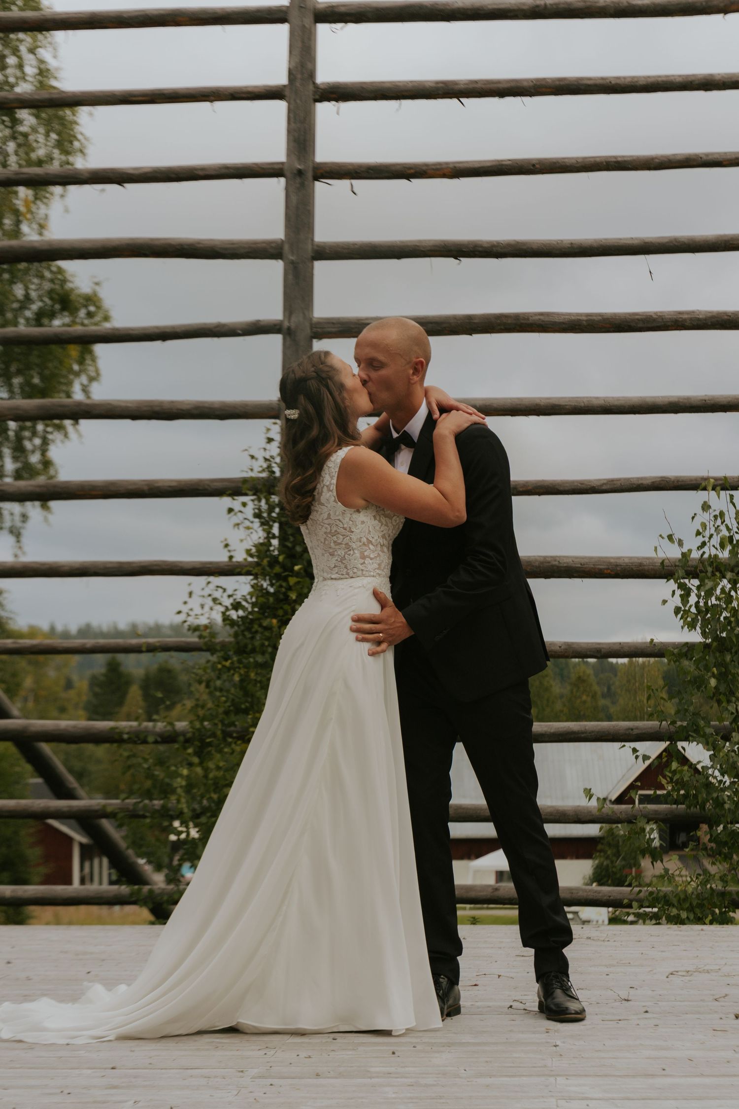 A couple shares a tender moment during their wedding ceremony on an outdoor wooden deck surrounded by railings.