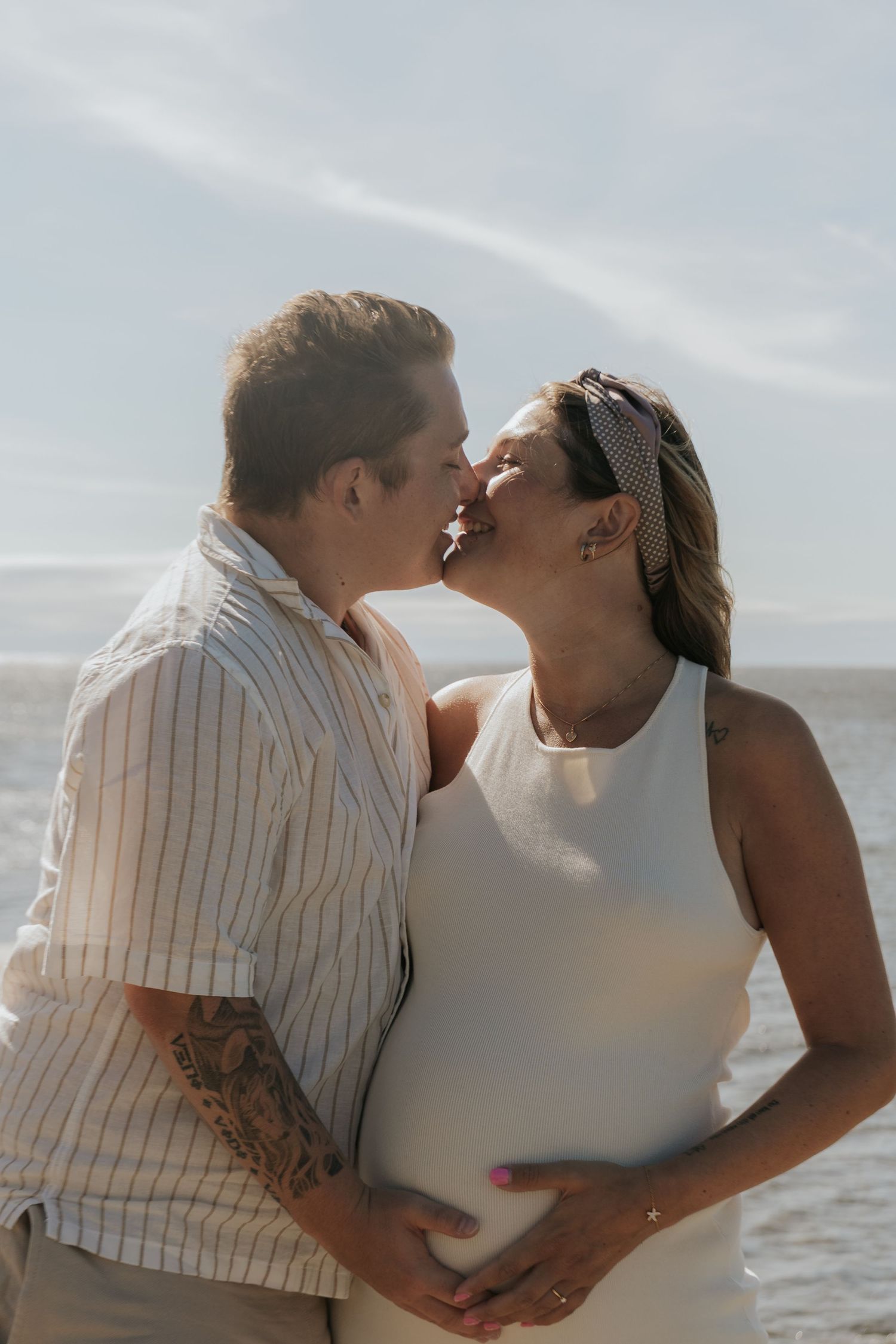 Intimate beach maternity photos with couple sharing tender moment by ocean.