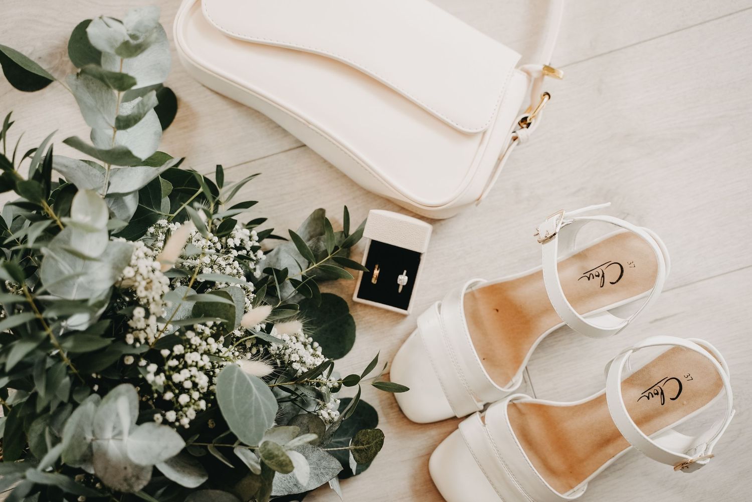 Elegant wedding details featuring white heels, greenery, and delicate floral arrangements on a light background.