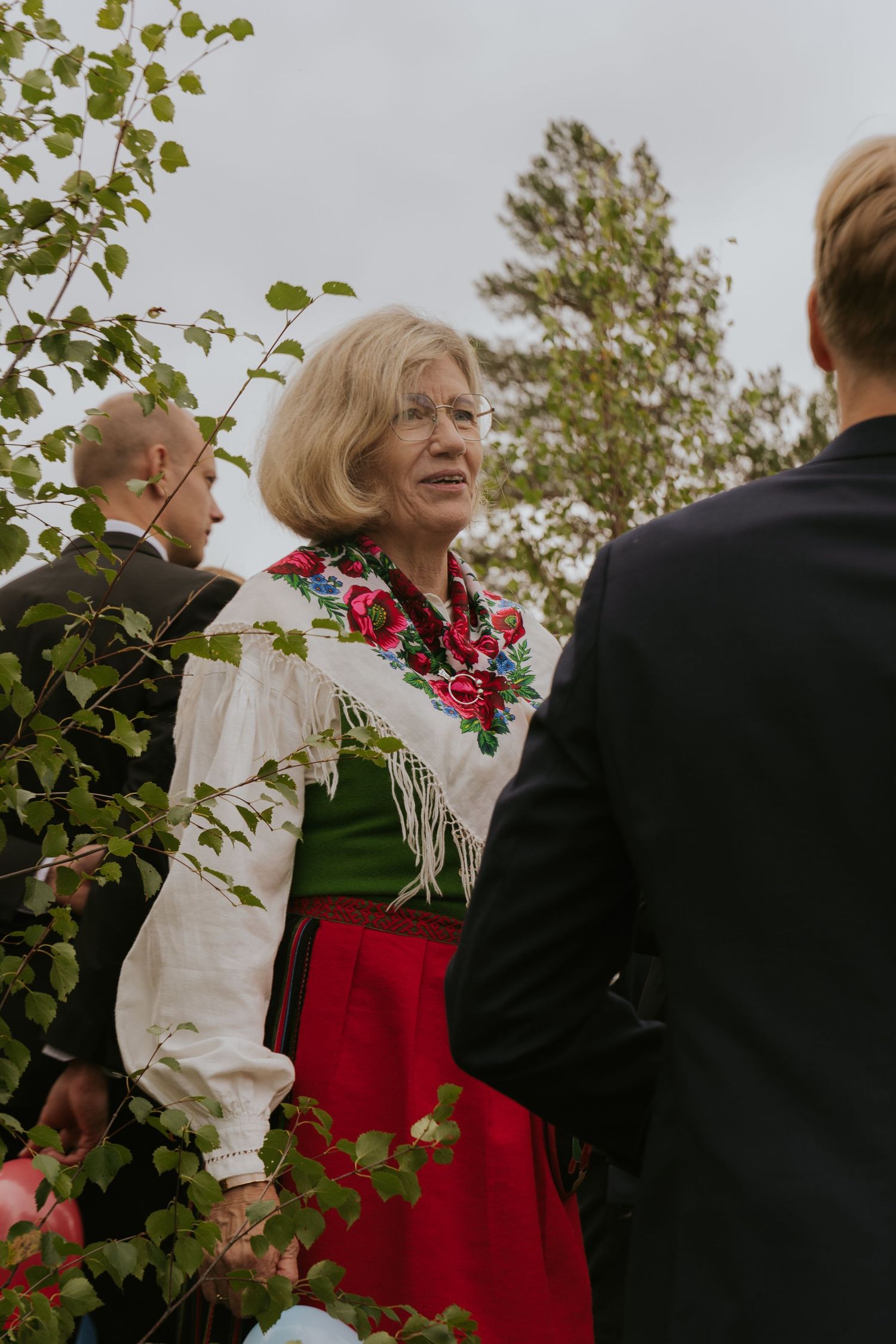 A group of people gather outdoors wearing formal attire with red and white clothing against a natural backdrop.