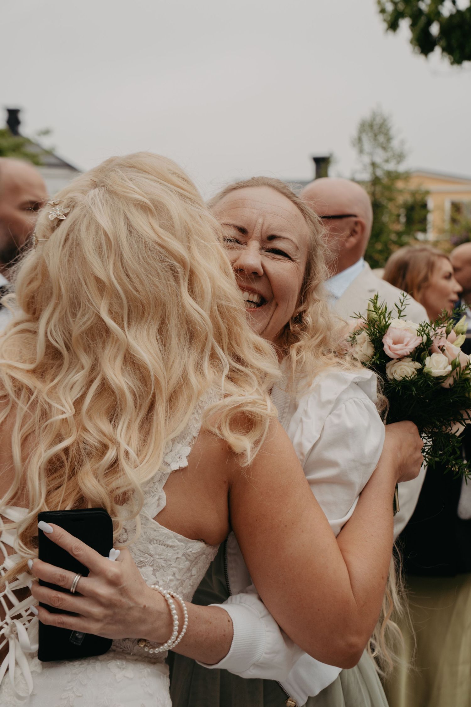 Emotional wedding guests share warm embraces and smiles during an outdoor celebration.