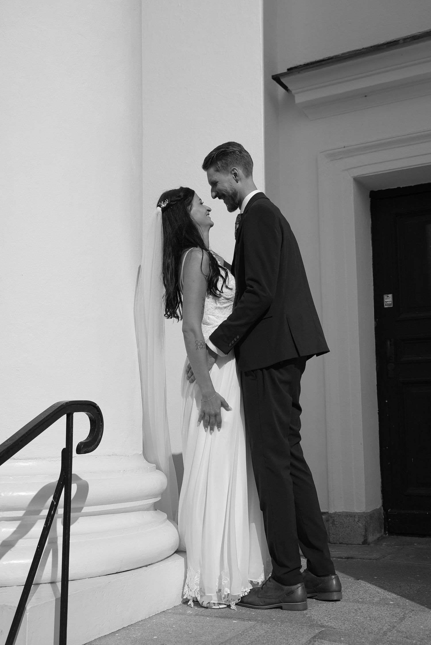 A couple in wedding attire share a playful moment together against white pillars in a series of black and white photos.