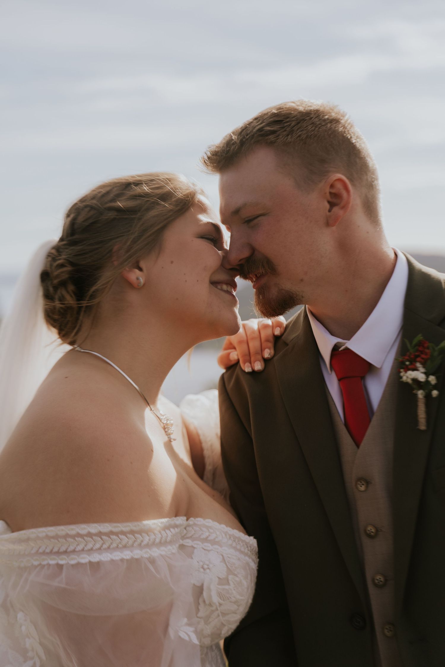 Close-up wedding portraits showing tender moments between bride in lace dress and groom with red tie.