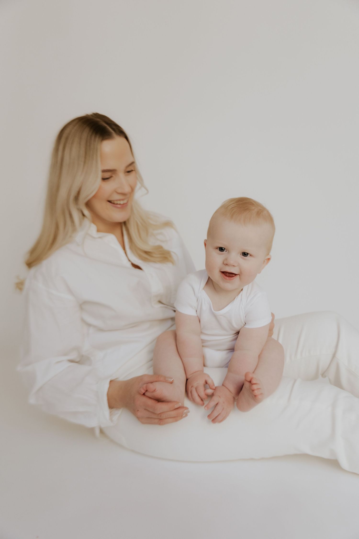 A tender moment between parent and infant dressed in white sitting together on a light background.